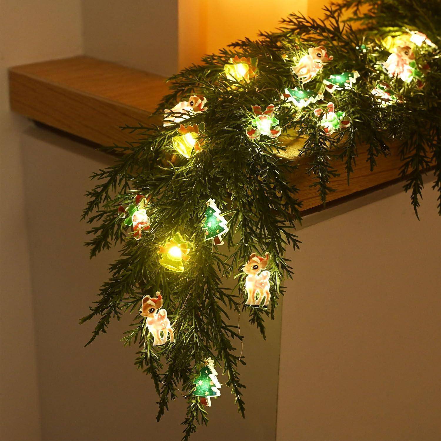 Immergrüne Girlande mit leuchtenden Rentier-förmigen Lichterketten, die über ein Holzregal im Innenbereich drapiert sind.
