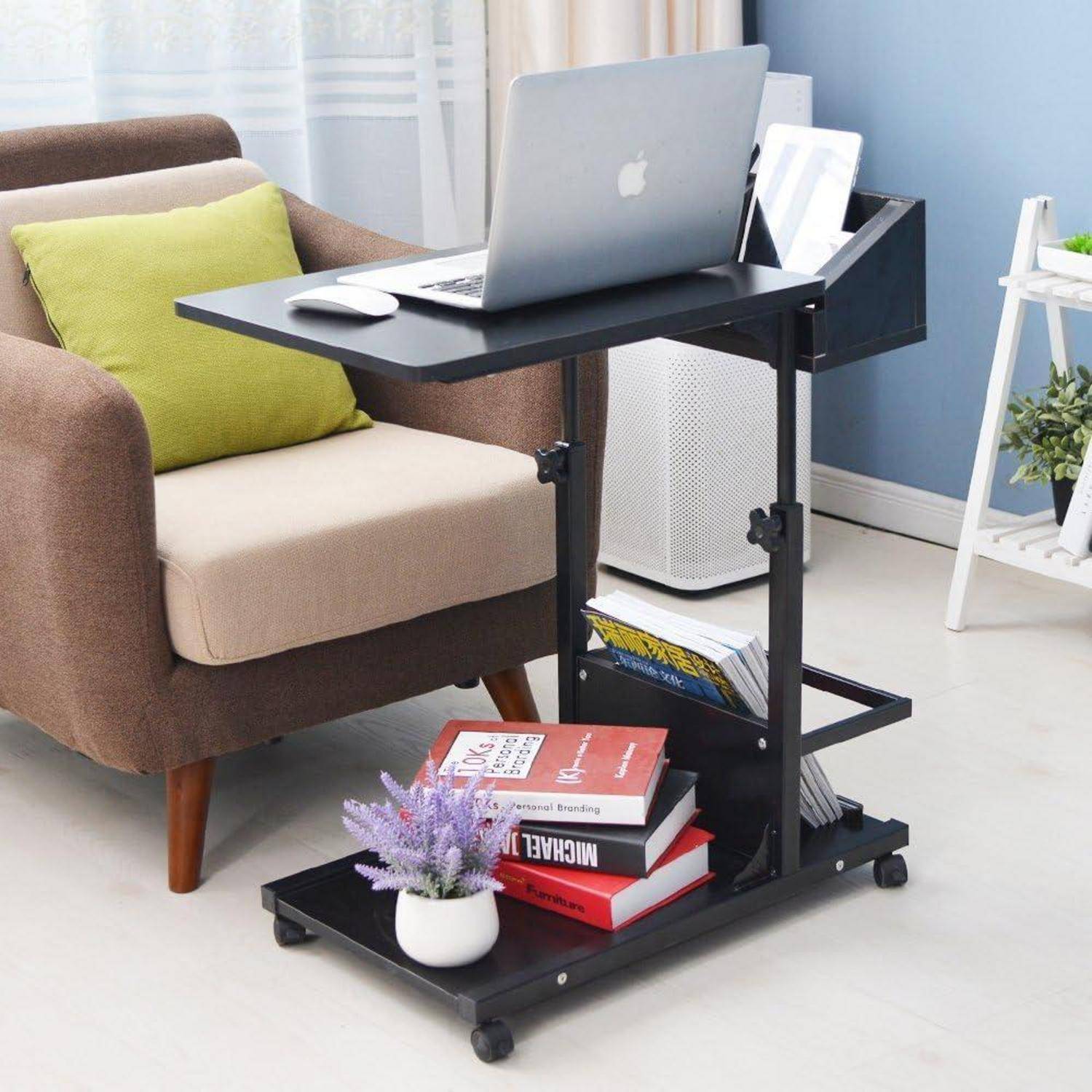 Verstellbarer fahrbarer Laptoptisch neben einem Sessel, mit einem Laptop, einer Maus, Büchern und einer kleinen Pflanze auf dem unteren Regal.