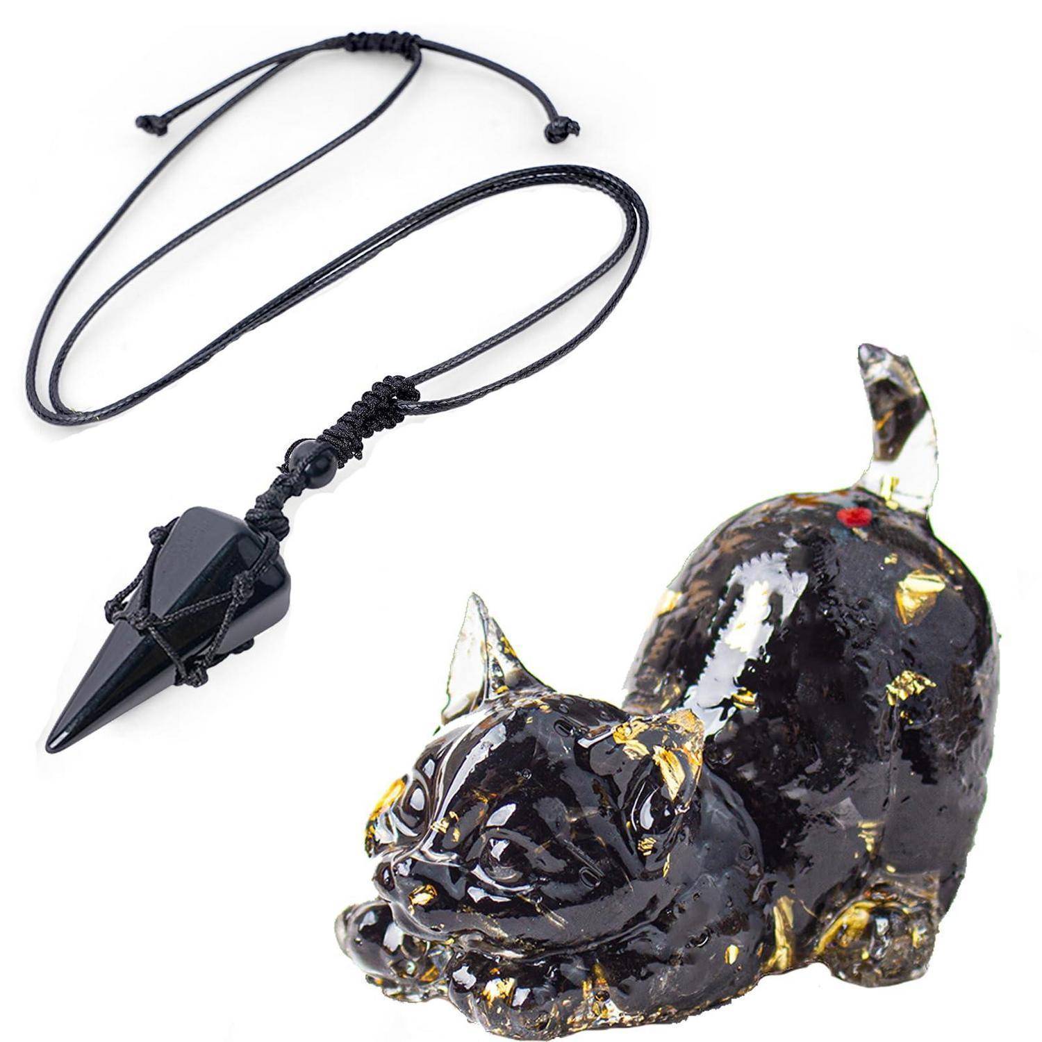 Schwarze Kristallanhängerkette mit spitzem Anhänger neben einer glänzenden schwarz-goldenen Katzenfigur auf weißem Hintergrund.