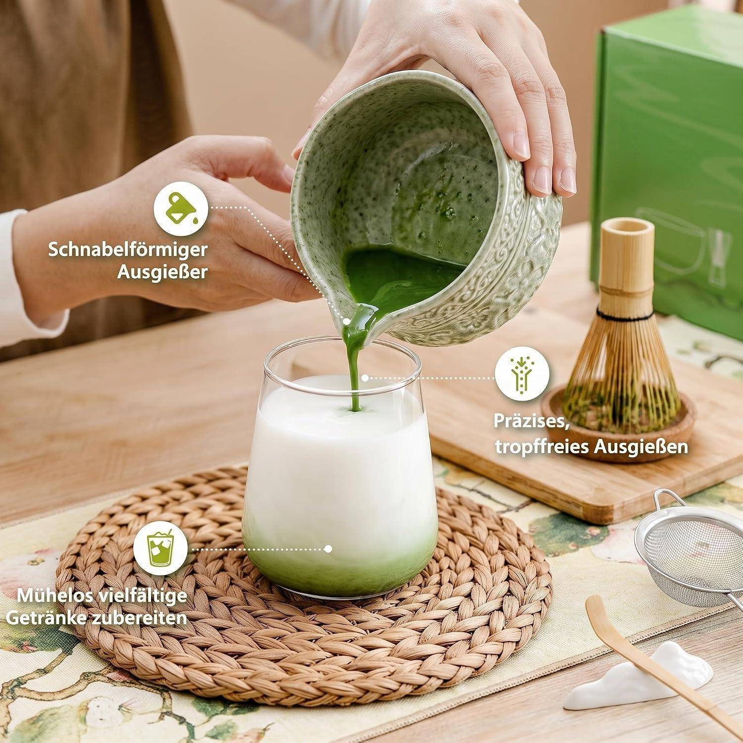 Hände gießen grünes Matcha aus einer Schale mit Ausguss in ein Glas Milch auf einem gewebten Platzset, mit deutschen Beschriftungen, die spritzerfreies Eingießen und vielseitige Getränkezubereitung hervorheben.