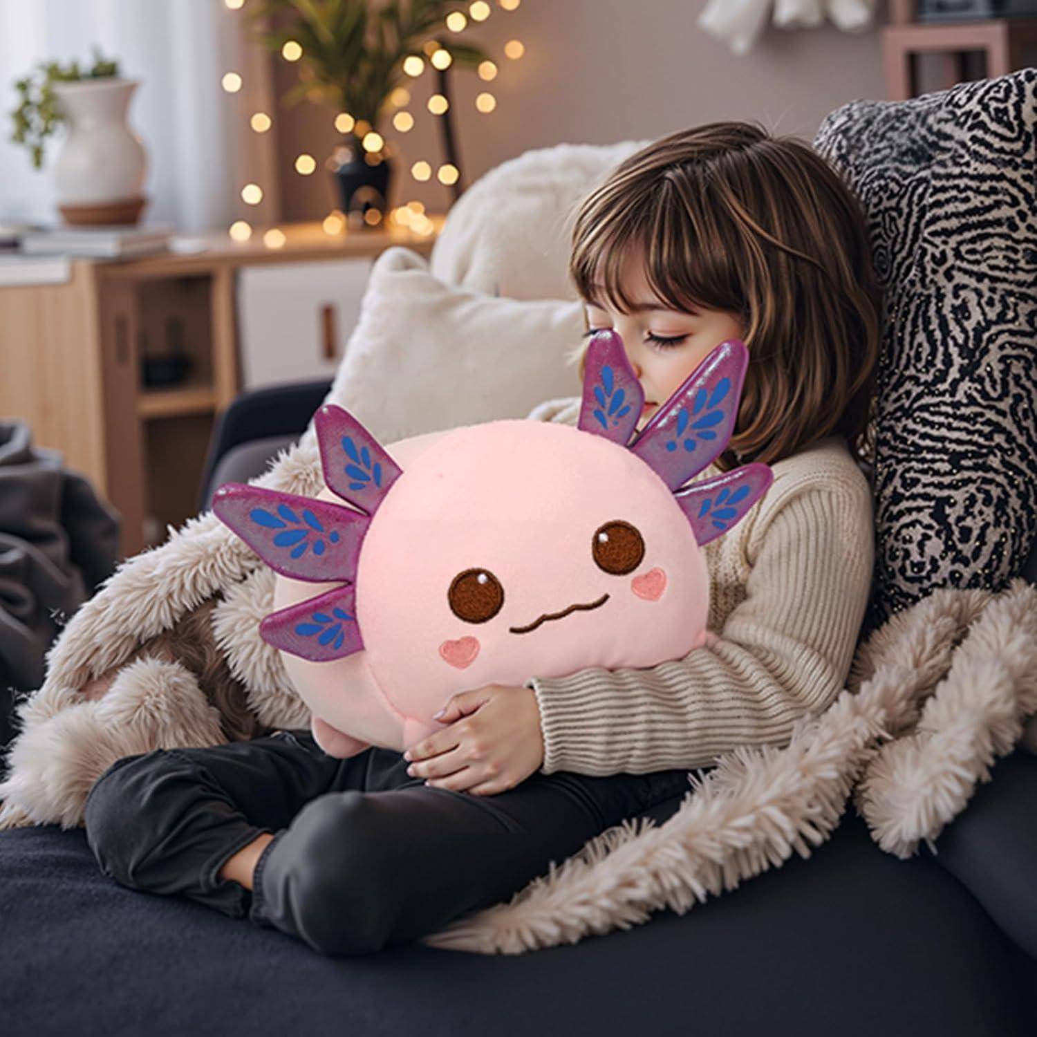Ein kleines Kind sitzt auf einem Sofa und umarmt ein rosa Axolotl-Kuscheltier in einem gemütlichen Wohnzimmer.
