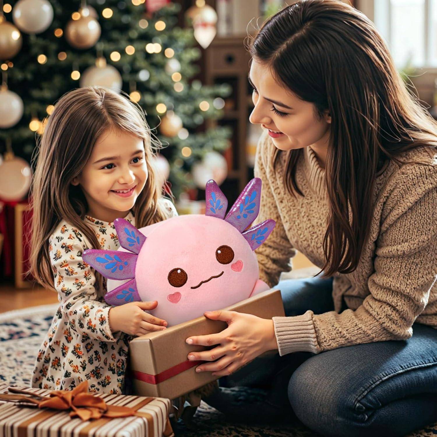 Frau und junges Mädchen lächeln, während sie eine Geschenkbox mit einem rosa Plüschtier mit violetten Flügeln austauschen, in einem dekorierten Wohnzimmer neben einem Weihnachtsbaum.