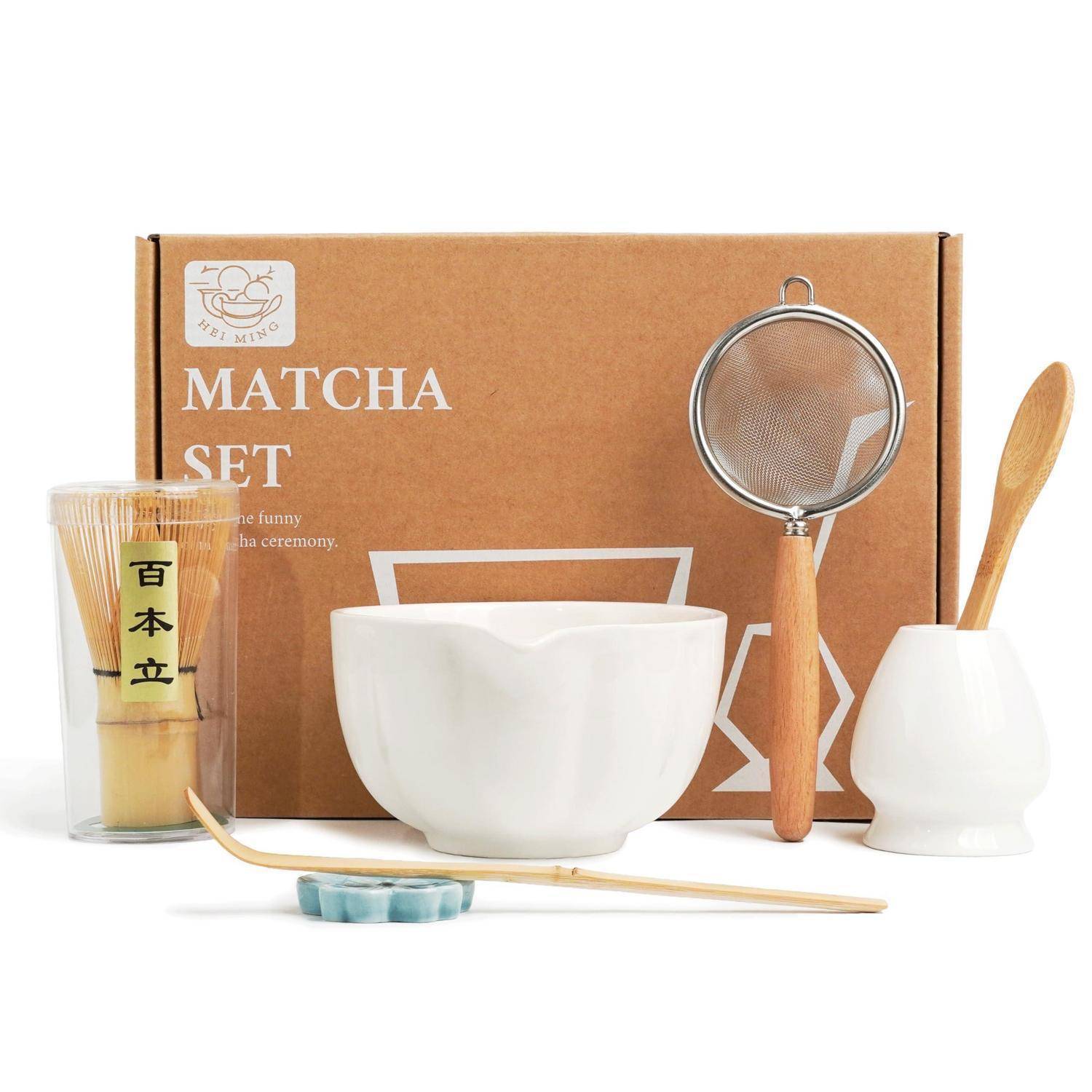 Matcha-Set mit Box, weiße Teeschale, Bambusquast, Sieb, Löffel, Löffel und Halter auf weißem Hintergrund angeordnet.