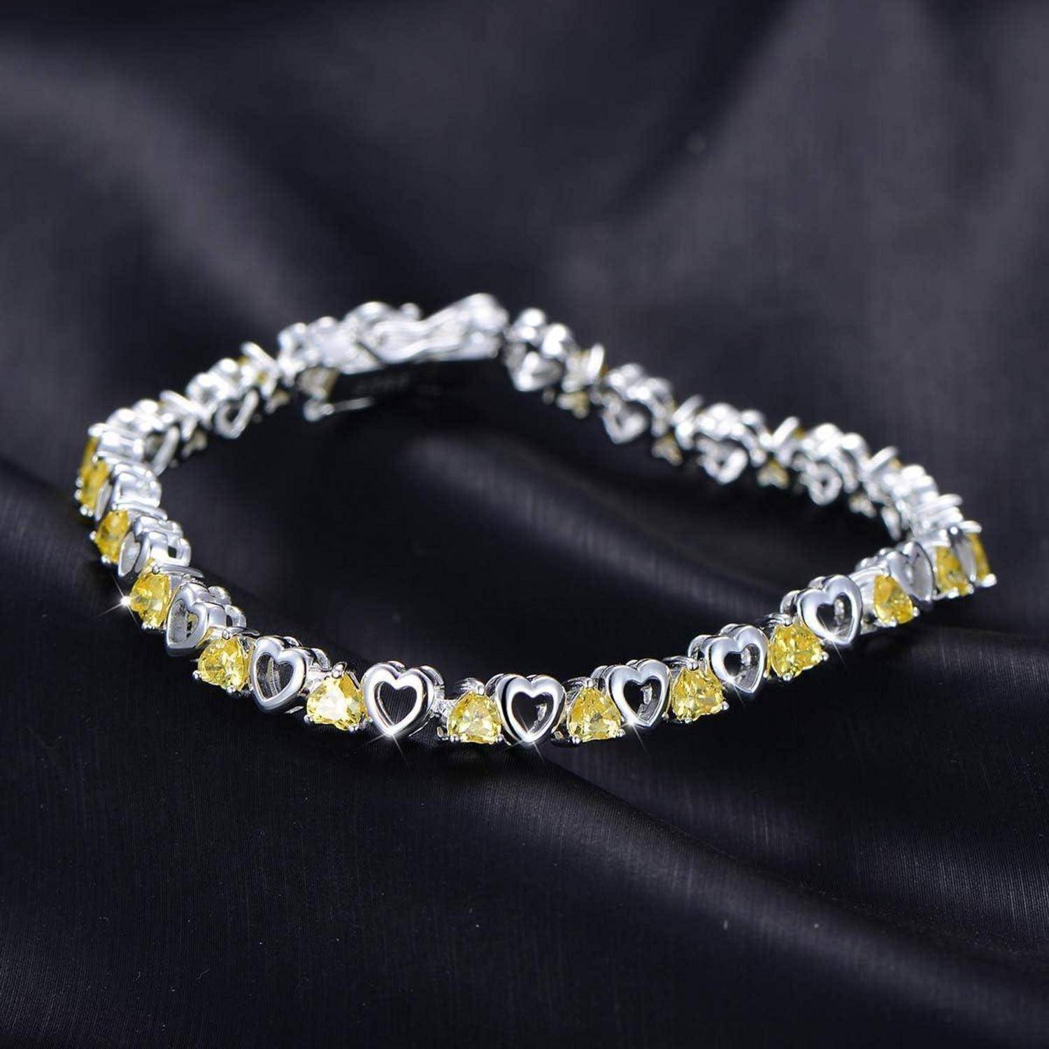 Silbernes Herz-Gliedarmband mit gelben Edelsteinen auf schwarzem Stoff-Hintergrund.