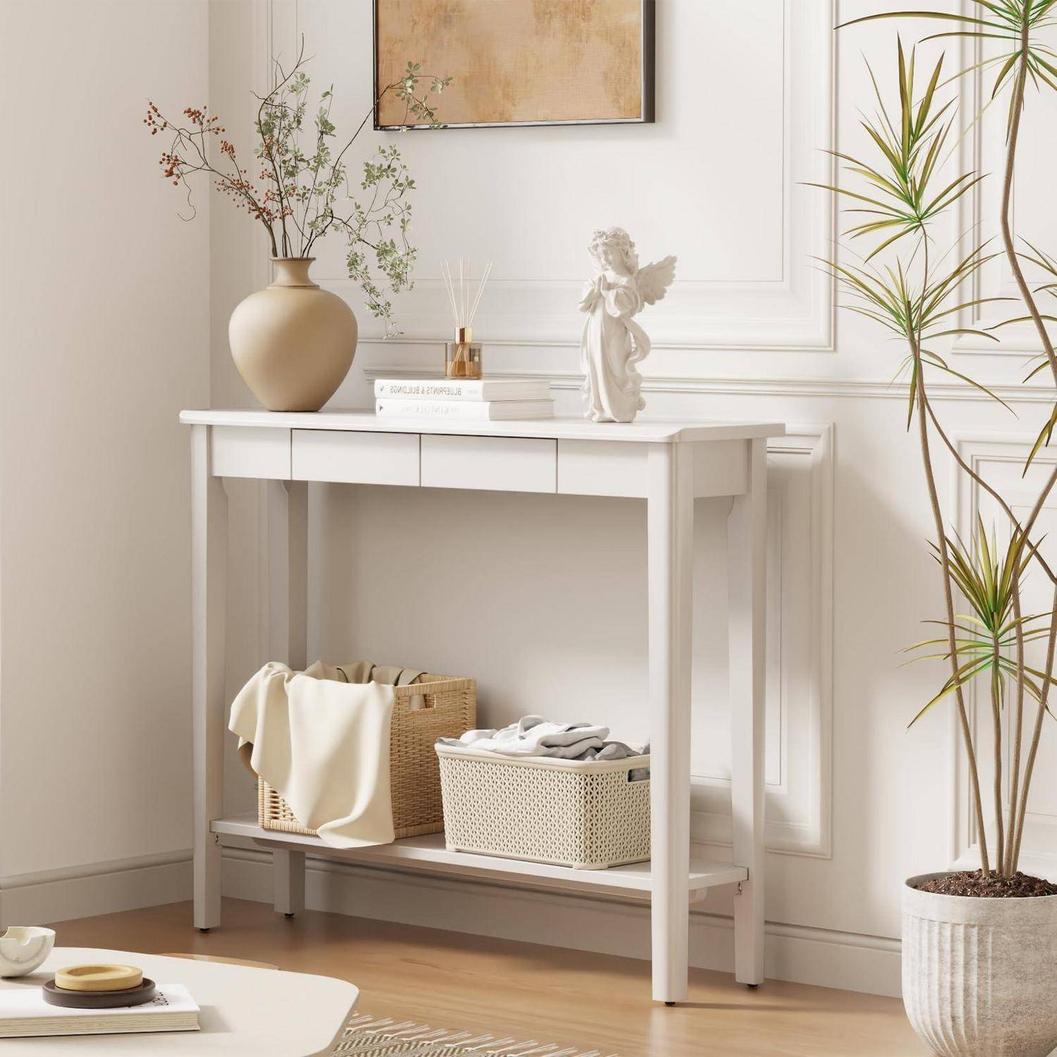 Stilvoller Konsolentisch mit Vase, Büchern, Engel-Figur, geflochtenen Körben und Topfpflanzen in einem hellen, minimalistischen Raum.
