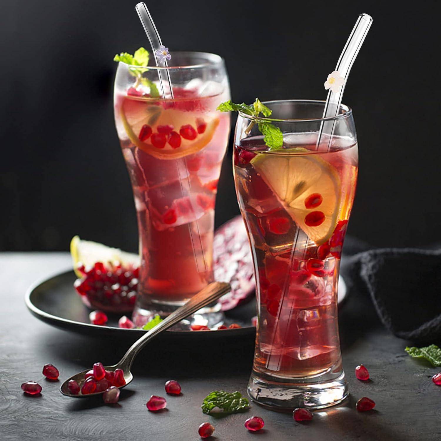 Zwei hohe Gläser mit rotem Fruchtsaftgetränk mit Zitronenscheiben, Minze und Strohhalmen, serviert auf einem dunklen Tisch mit Granatapfelkernen und einer Zitronenspalte.