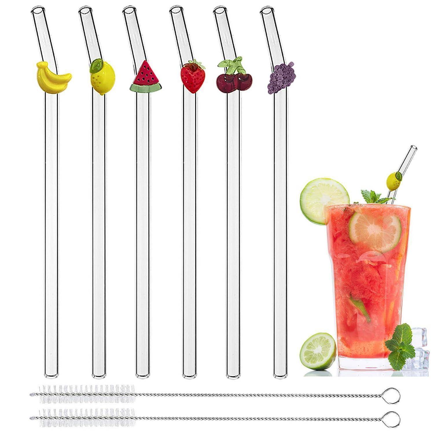 Satz aus sechs Glas-Trinkhalmen mit Fruchtaufsätzen und drei Reinigungsbürsten neben einem roten Zitruscocktail mit Limettengarnierung.