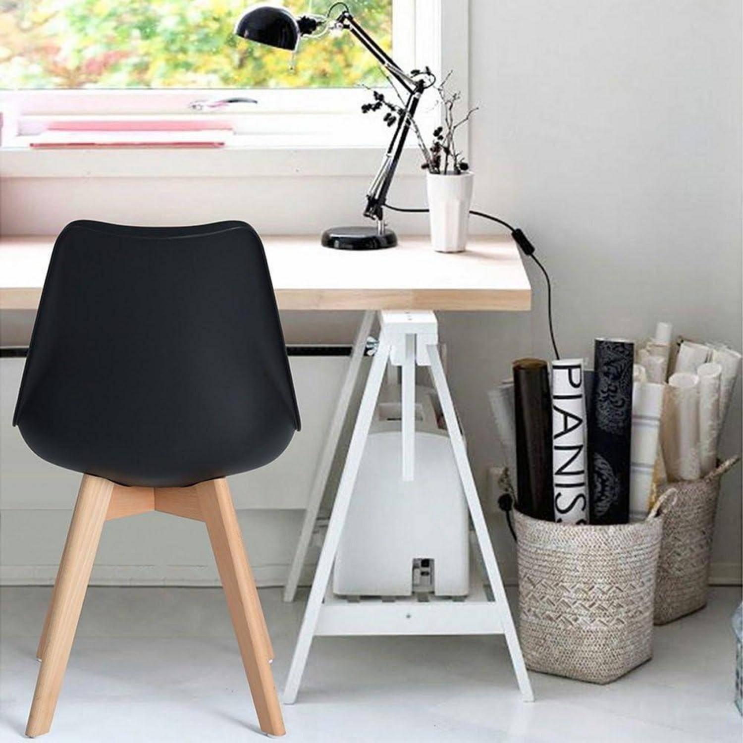 Minimalistisches Home-Office mit schwarzem Stuhl an einem weißen Schreibtisch, schwarzer Schreibtischlampe und Topfpflanze, daneben ein Korb mit aufgerollten Papieren und Magazinen.