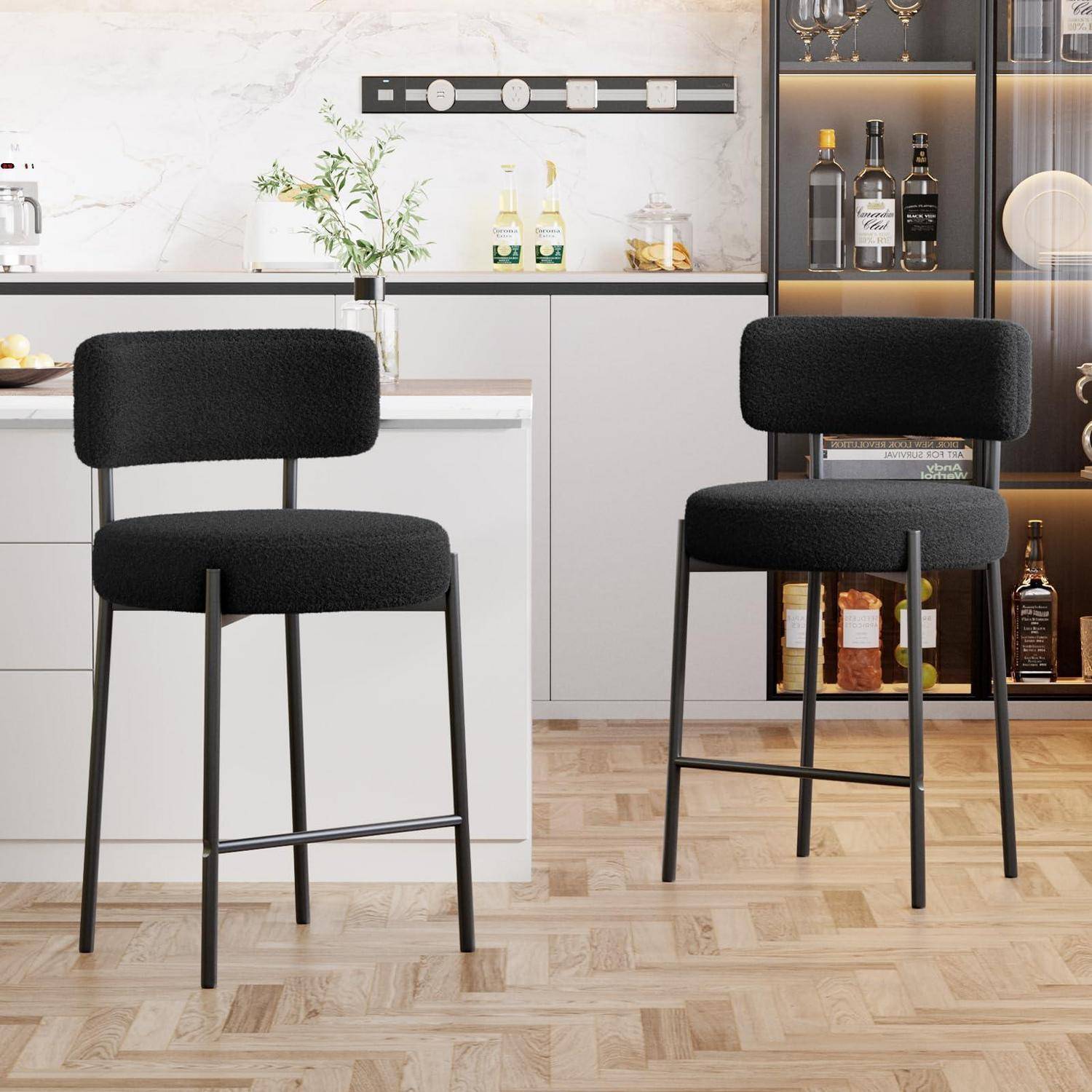 Moderne Küche mit zwei schwarz gepolsterten Barhockern vor einer weißen Insel und beleuchtetem Glassschrank mit Flaschen.