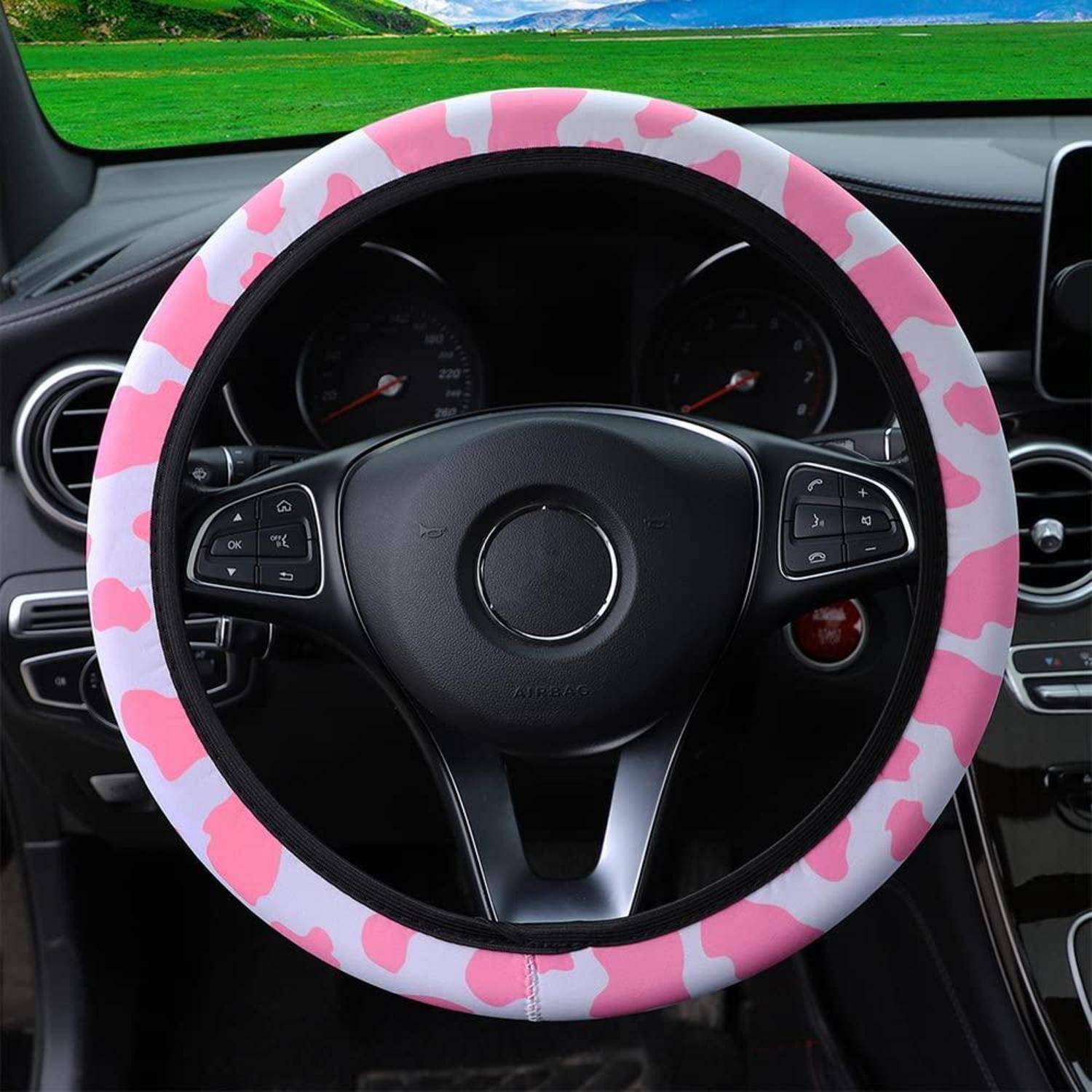 Autolenkrad mit einem rosa Herzchen-Muster-Überzug in einem Fahrzeug, aus dem Fahrersitz fotografiert.