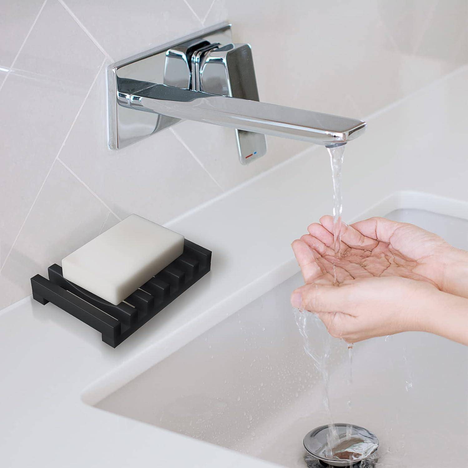 Wandmontierten Chrome-Wasserhahn mit fließendem Wasser in hohle Hände über einem Waschbecken, mit einem Seifenstück auf einem Halter daneben.