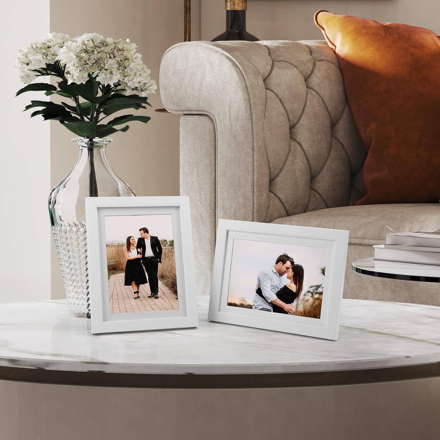 Ein Wohnzimmercouchtisch mit zwei eingerahmten Paarfotos, einer Vase mit weißen Blumen, gestapelten Büchern und einem beigen Sofa mit einem orangefarbenen Kissen.