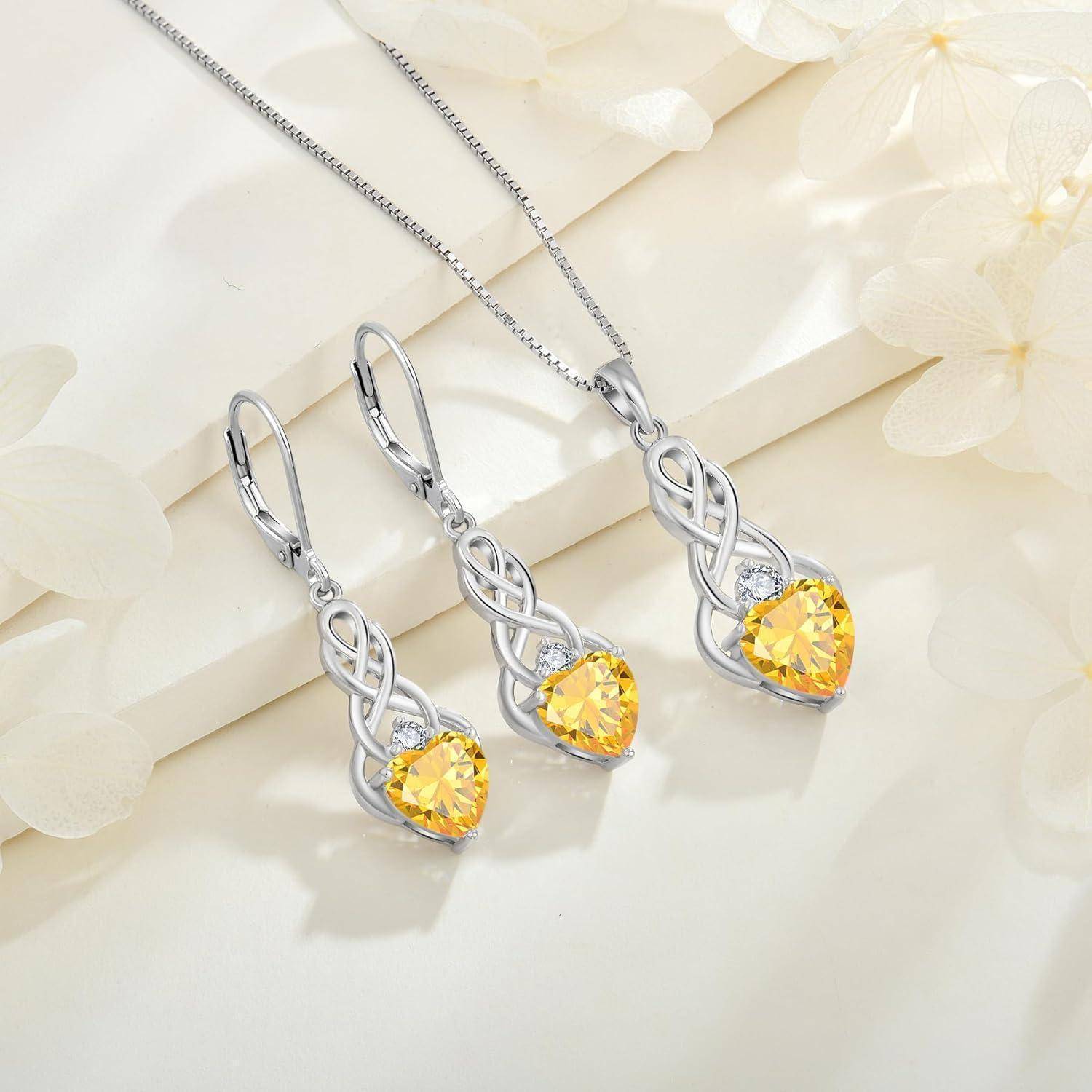 Silbernes herzförmiges Schmuckset mit passendem Ohrringe und Halskette, jeweils mit gelbem Edelsteinanhänger auf hellem Blumenhintergrund.