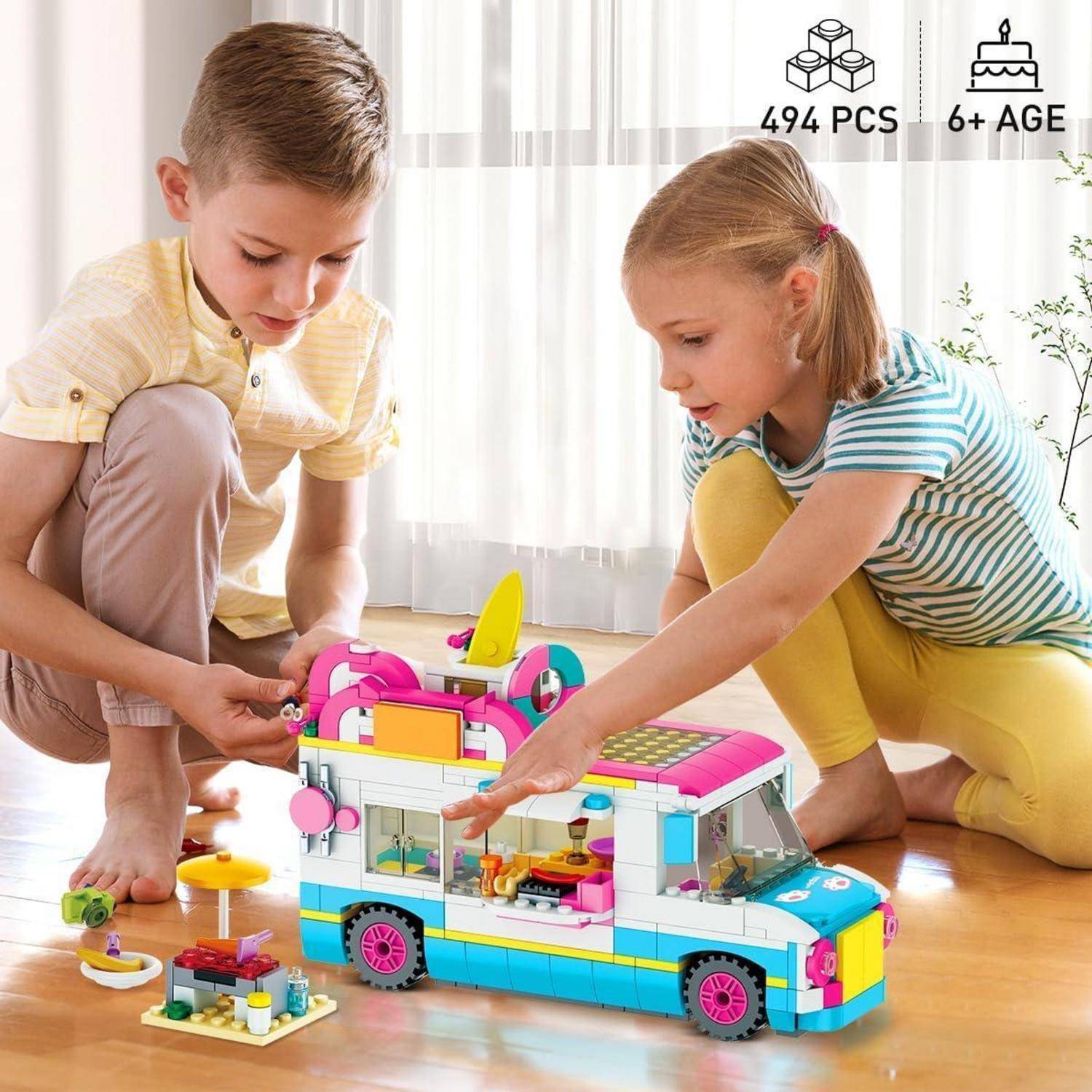 Zwei Kinder spielen auf dem Boden mit einem bunten LEGO-ähnlichen Campingbus-Bauset; Bildetiketten zeigen 