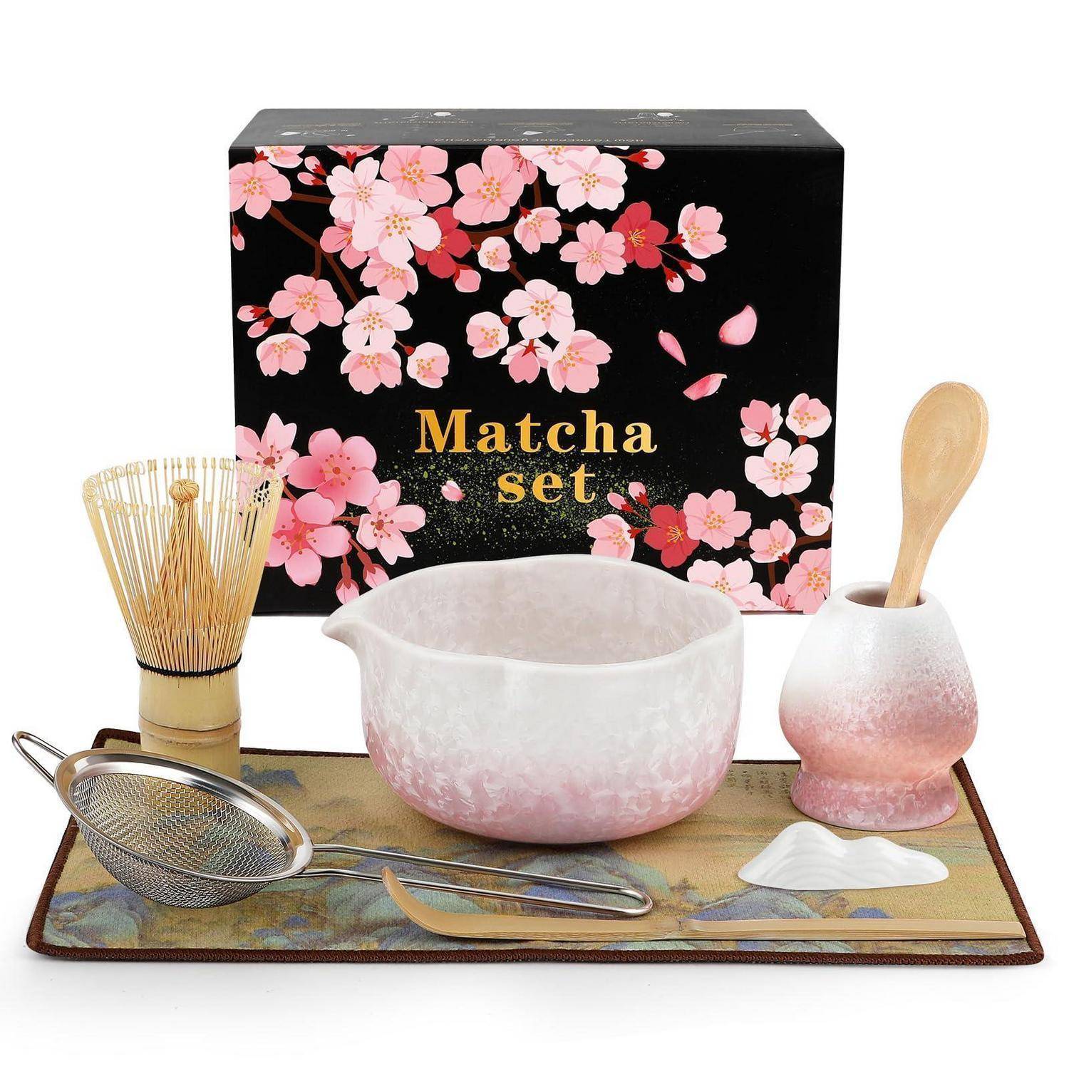 Matcha-Tee-Set mit dekorativer Schachtel, Schneebesen, Schale, Löffel, Sieb und Tablett auf weißem Hintergrund angeordnet.