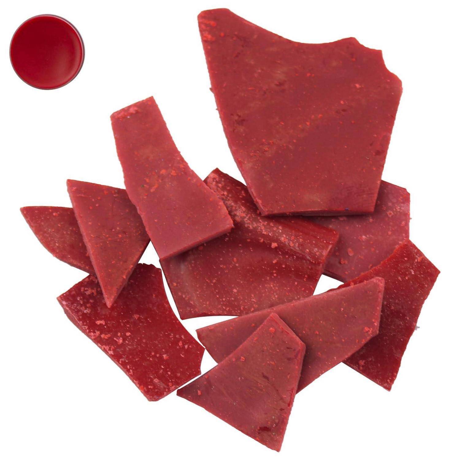 Verstreute rote Scherben aus zerbrochenem Material auf weißem Hintergrund, mit einer kleinen roten kreisförmigen Kappe oder einem Deckel oben links.