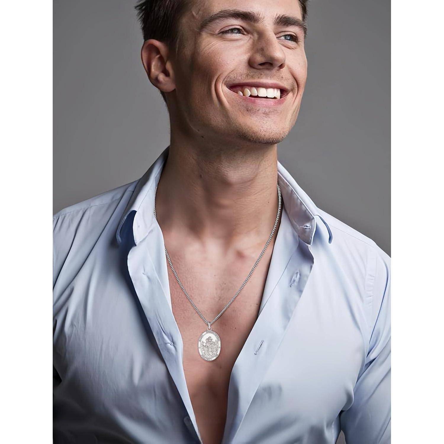 Porträt eines lächelnden jungen Mannes in einem offenen hellblauen Hemd, der eine silberne Anhängerkette um den Hals trägt, vor einem einfarbig grauen Hintergrund.