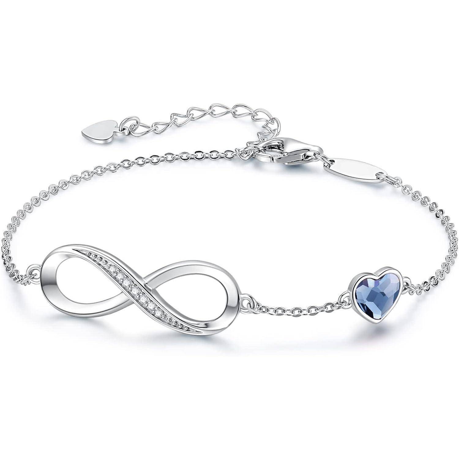 Silbernes Armband mit Unendlichkeitsanhänger und blauem herzförmigem Edelstein in der Mitte auf weißem Hintergrund.