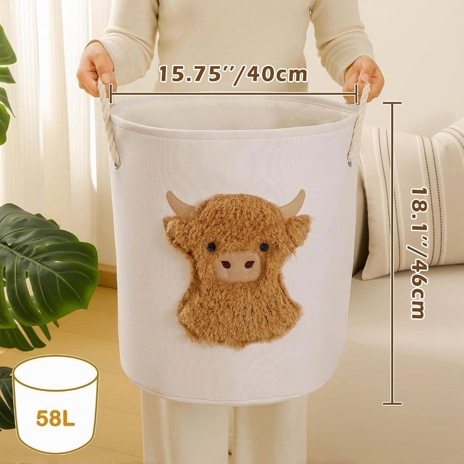 Person hält einen weißen Stofflagerbehälter mit einem Plüsch-Kuhgesicht; gekennzeichnet mit 15,75 Zoll/40 cm Breite, 18,1 Zoll/46 cm Höhe, 58 L Kapazität.