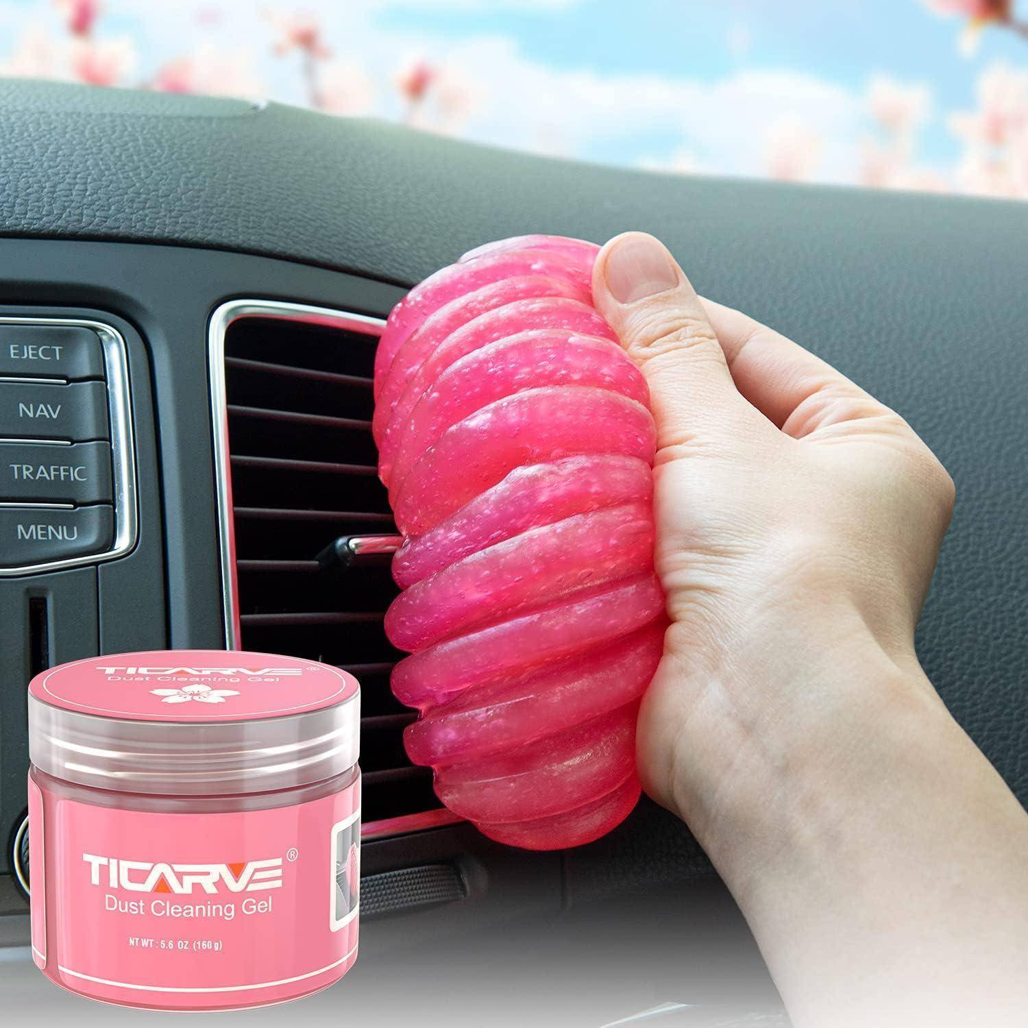 Hand verwendet rosa Reinigungsgel zum Entfernen von Staub aus einem Autolüftungsgitter, mit einem Ticarve Dust Cleaning Gel Glas in der Ecke.