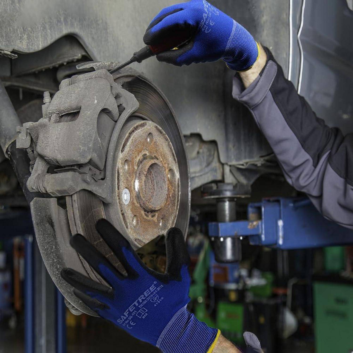 Mechaniker mit blauen Handschuhen arbeitet in einer Werkstatt an der vorderen Bremsscheibe und dem Bremssattel eines Autos.