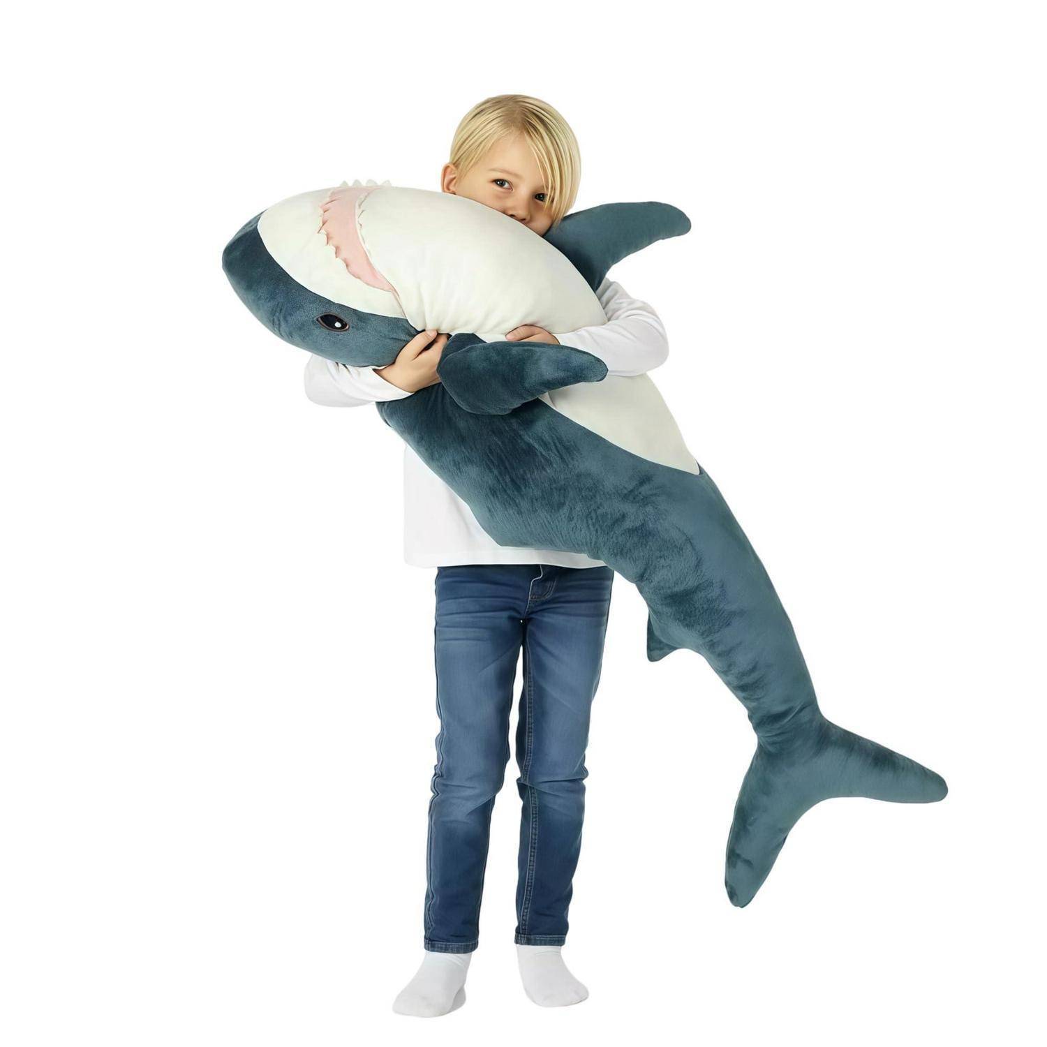 Kleines Kind auf weißem Hintergrund, das ein großes blau-weiß gestreiftes Kuscheltier-Hai umarmt.