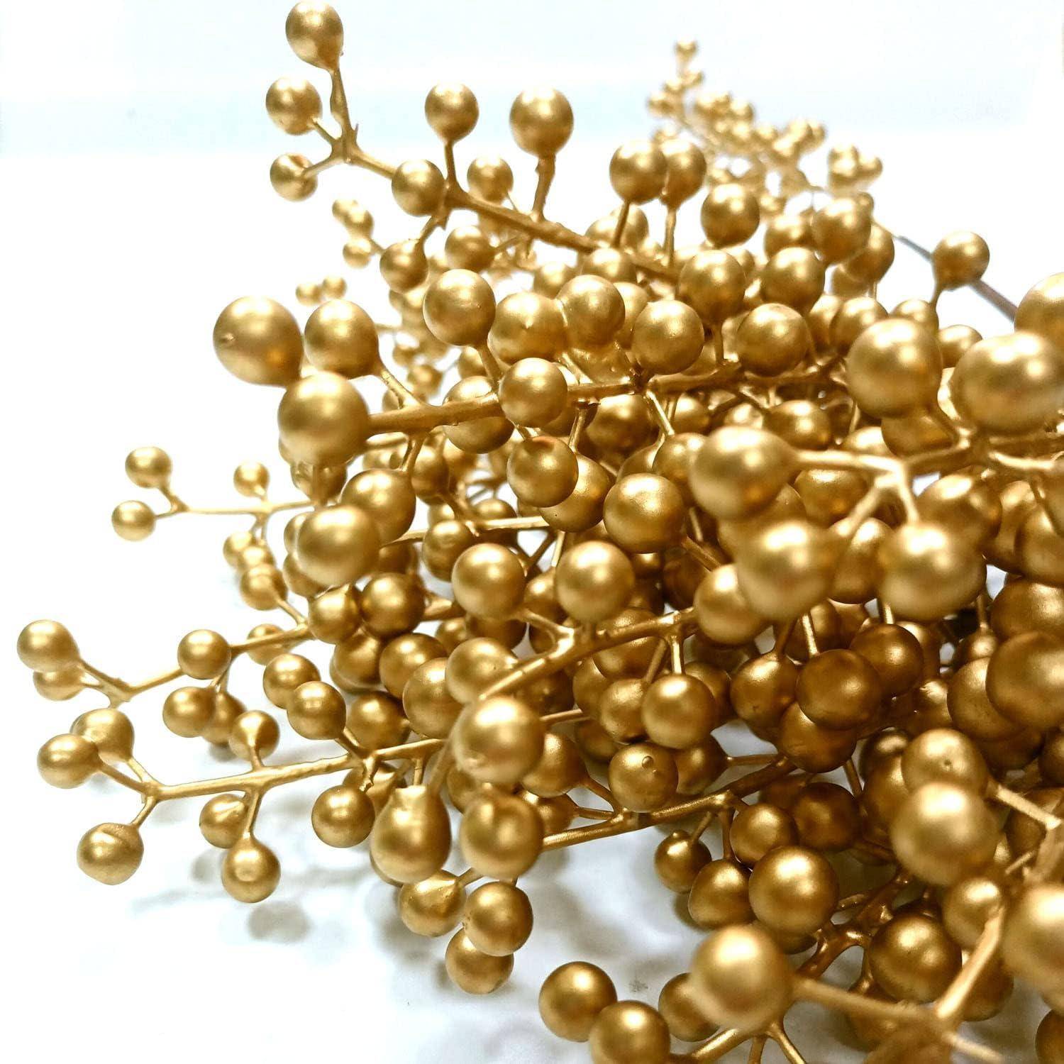 Nahaufnahme eines goldenen dekorativen Beerenzweigs mit vielen metallischen Perlentrauben auf dünnen Stielen vor weißem Hintergrund.