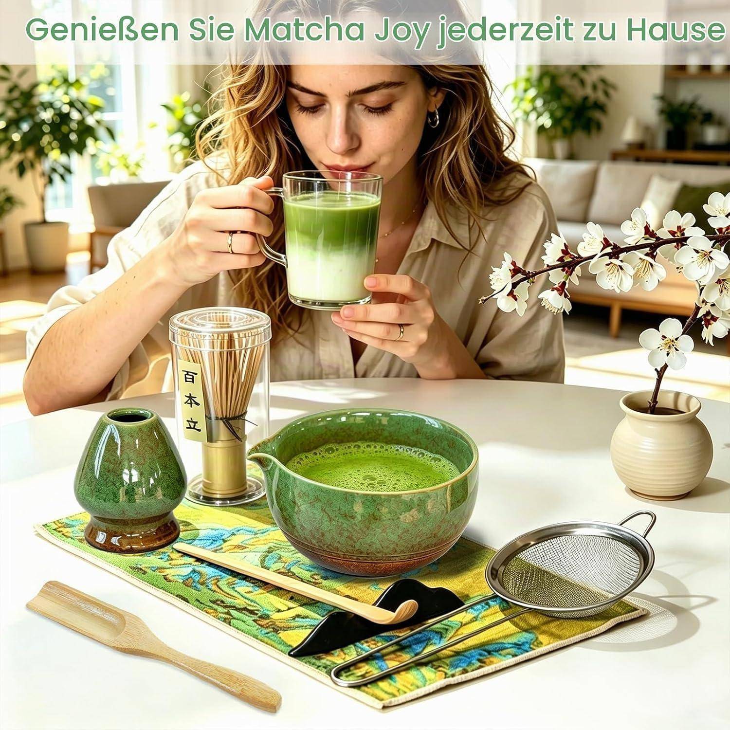 Frau zu Hause, die Matcha aus einer Glastasse trinkt, mit Matcha-Schüssel, Schneebesen, Sieb und Teeservice auf dem Tisch; der Text lautet „Genießen Sie Matcha Joy jederzeit zu Hause".