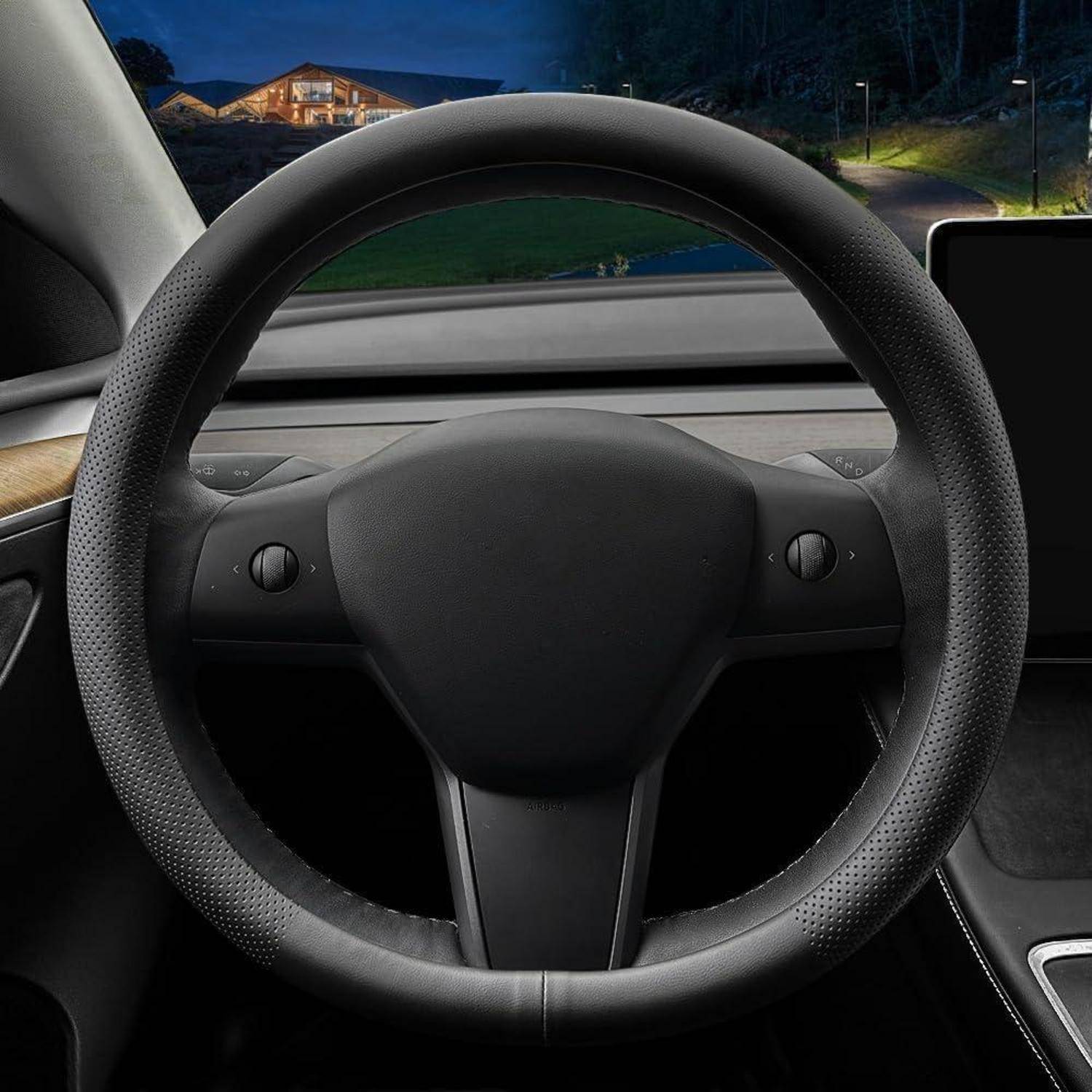 Innenaum eines Tesla-ähnlichen Autos mit rundem Lenkrad mit zentraler Nabe und zwei Steuertasten, Blick vom Fahrersitz bei Nacht mit einem Haus im Voraus sichtbar.