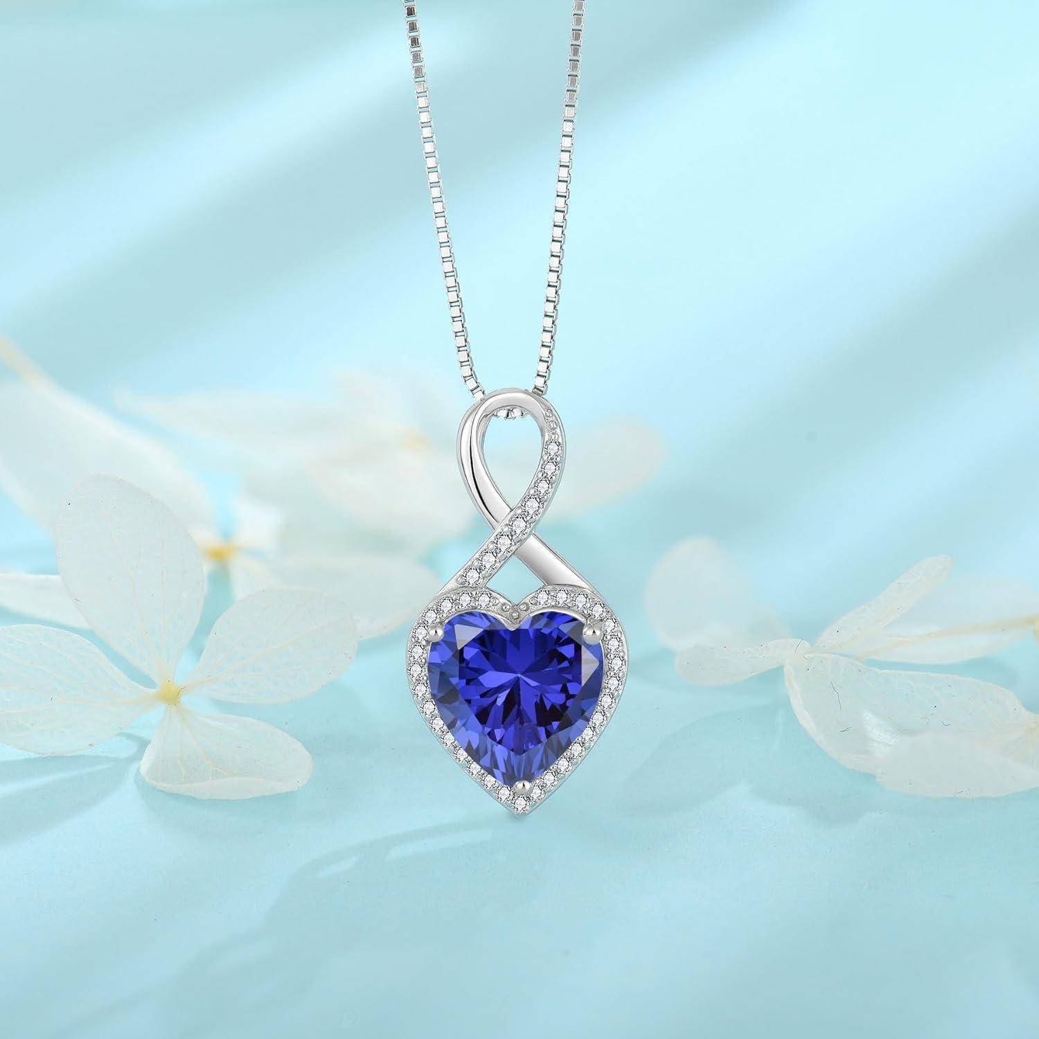 Silbernes Unendlichkeitsanhänger-Halskette mit herzförmigem blauem Edelstein und Halo aus klaren Steinen auf hellblauem Blumenhintergrund