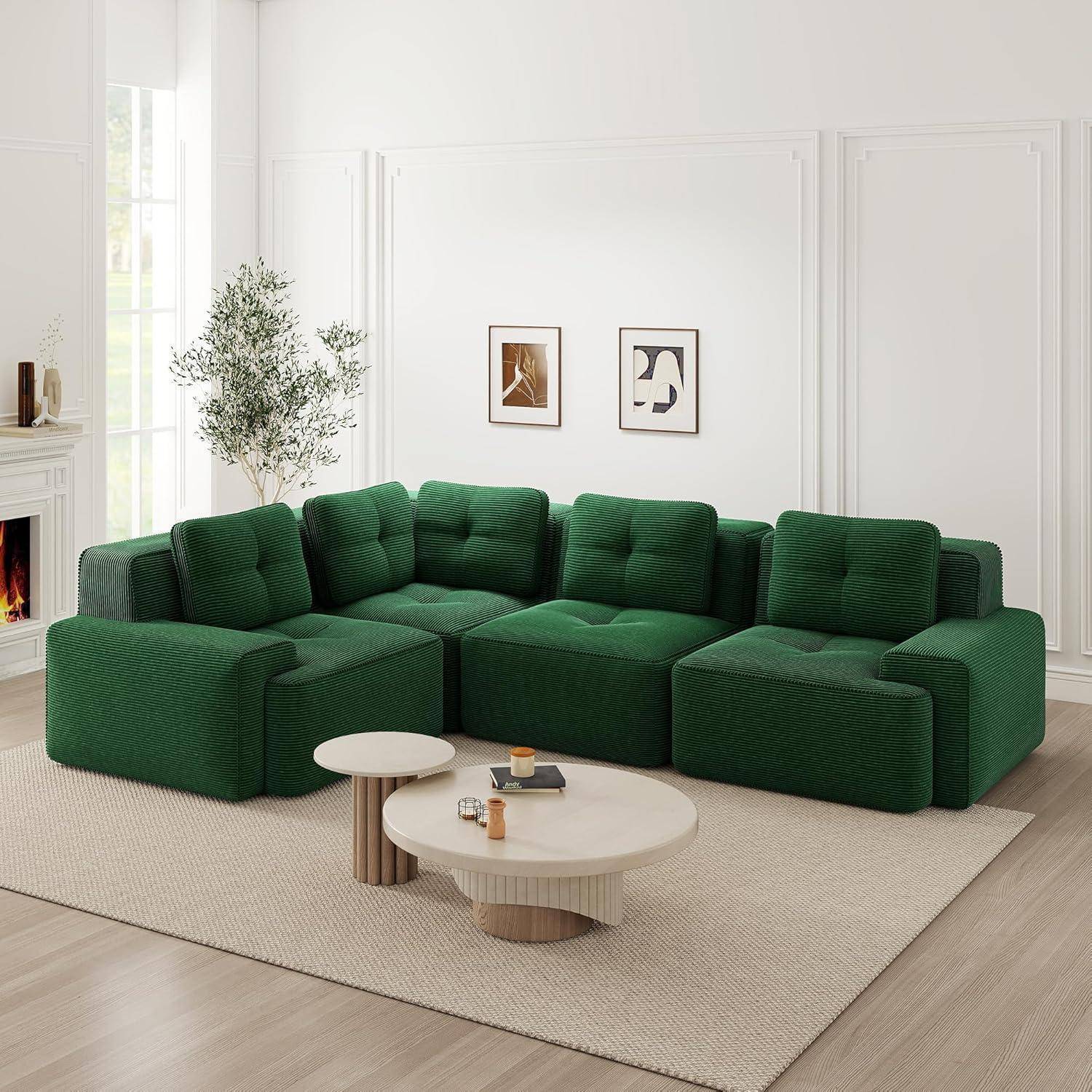 Modulares grünes Sofa in einem hellen, weiß eingerichteten Wohnzimmer mit zwei runden Couchtischen auf einem beigen Teppich und gerahmten Wandbildern dahinter.