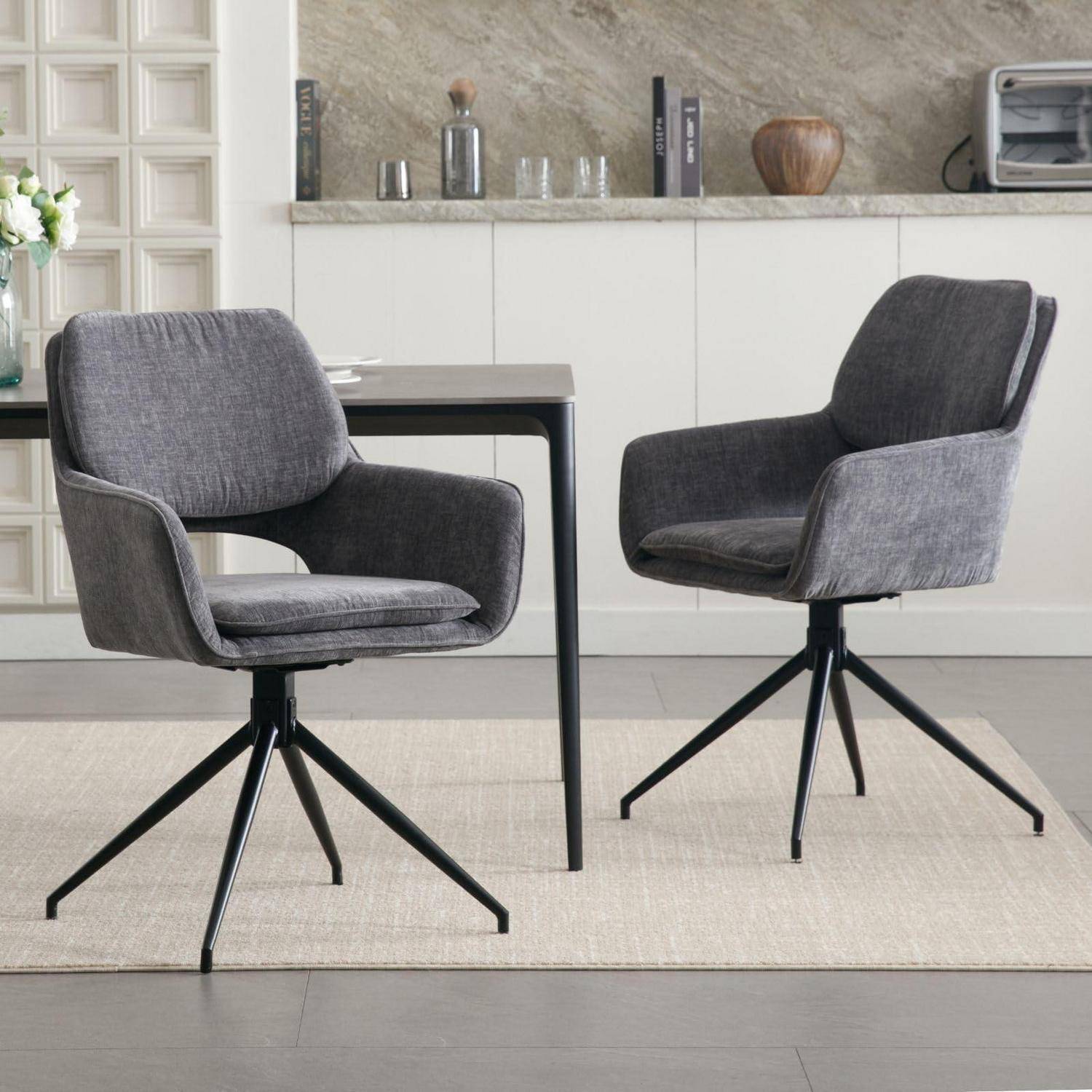Zwei grau gepolsterte Drehstühle mit schwarzen Metallbeinen sitzen auf einem hellen Teppich neben einem kleinen Tisch in einem modernen Raum.