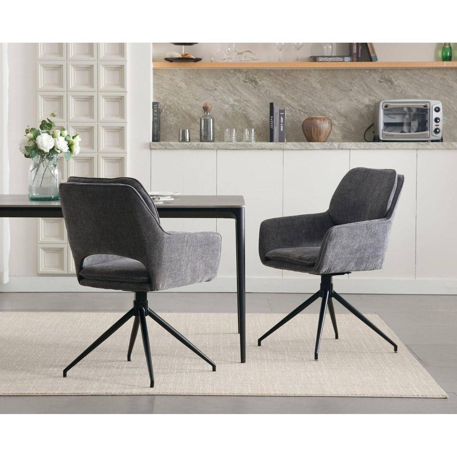 Zwei graue Drehstühle mit schwarzen Beinen neben einem dunklen Tisch in einem modernen Küchen-Essbereich mit weißen Schränken und einer Vase mit Blumen.