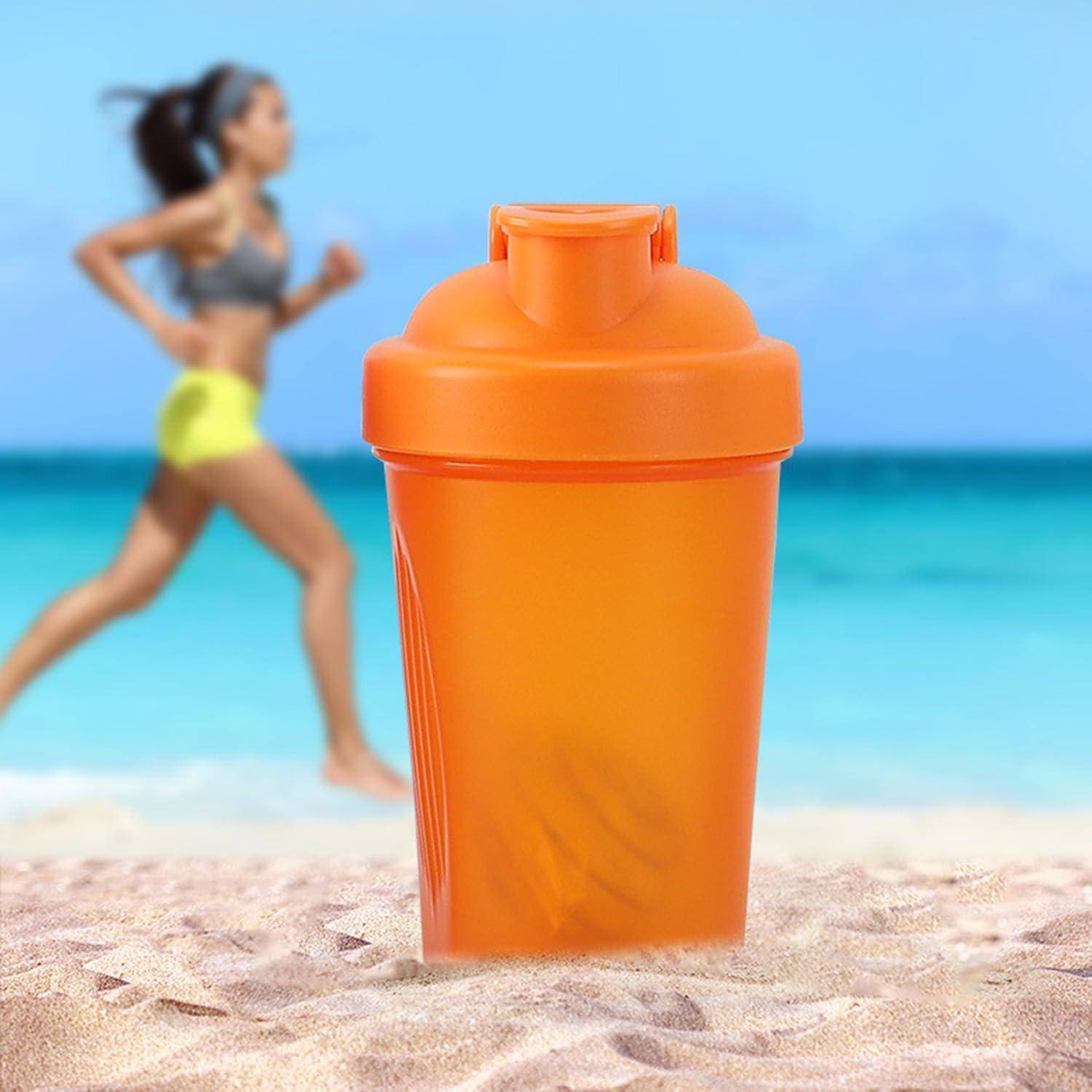 Orangener Protein-Shaker auf sandigem Strand mit unscharfer Frau, die im Hintergrund in der Nähe des Ozeans joggt.