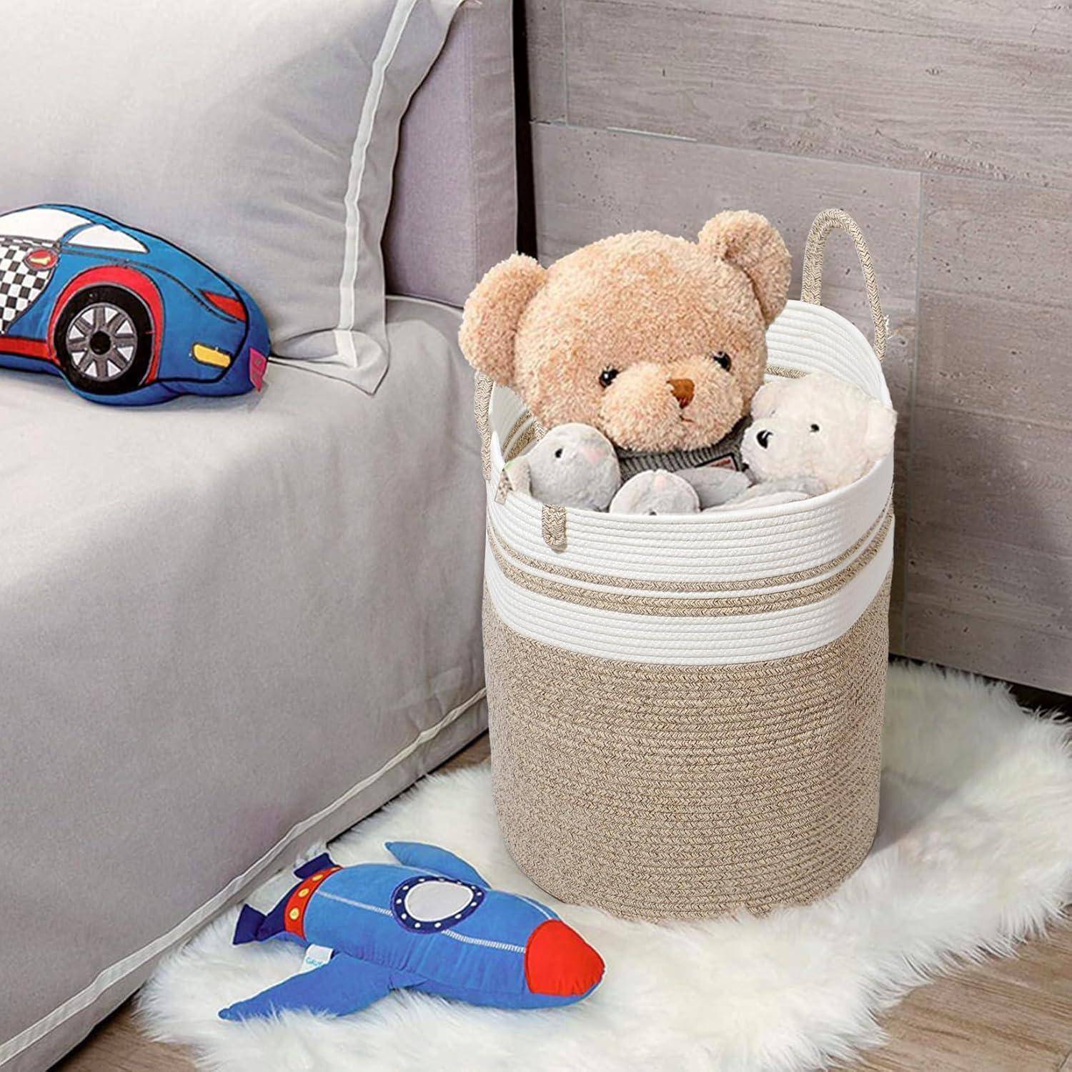 Ein weiches Spielzeug-Aufbewahrungskorb neben einem Bett, der Teddybären und Plüschtiere auf einem weißen Teppich hält, mit einem Autokissen und einem Rakettenspielzeug in der Nähe.