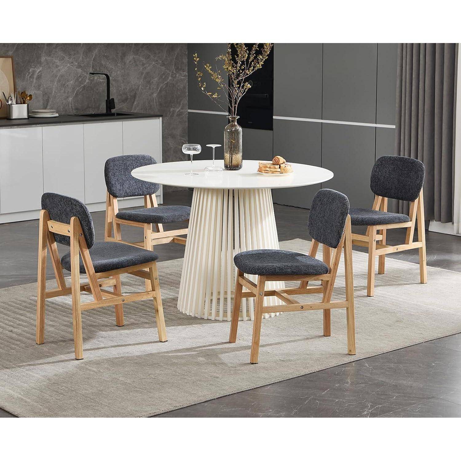 Modernes Esszimmer mit vier gepolsterten Holzstühlen um einen runden weißen Tisch mit einer Vase als Mittelstück auf einem hellen Teppich.
