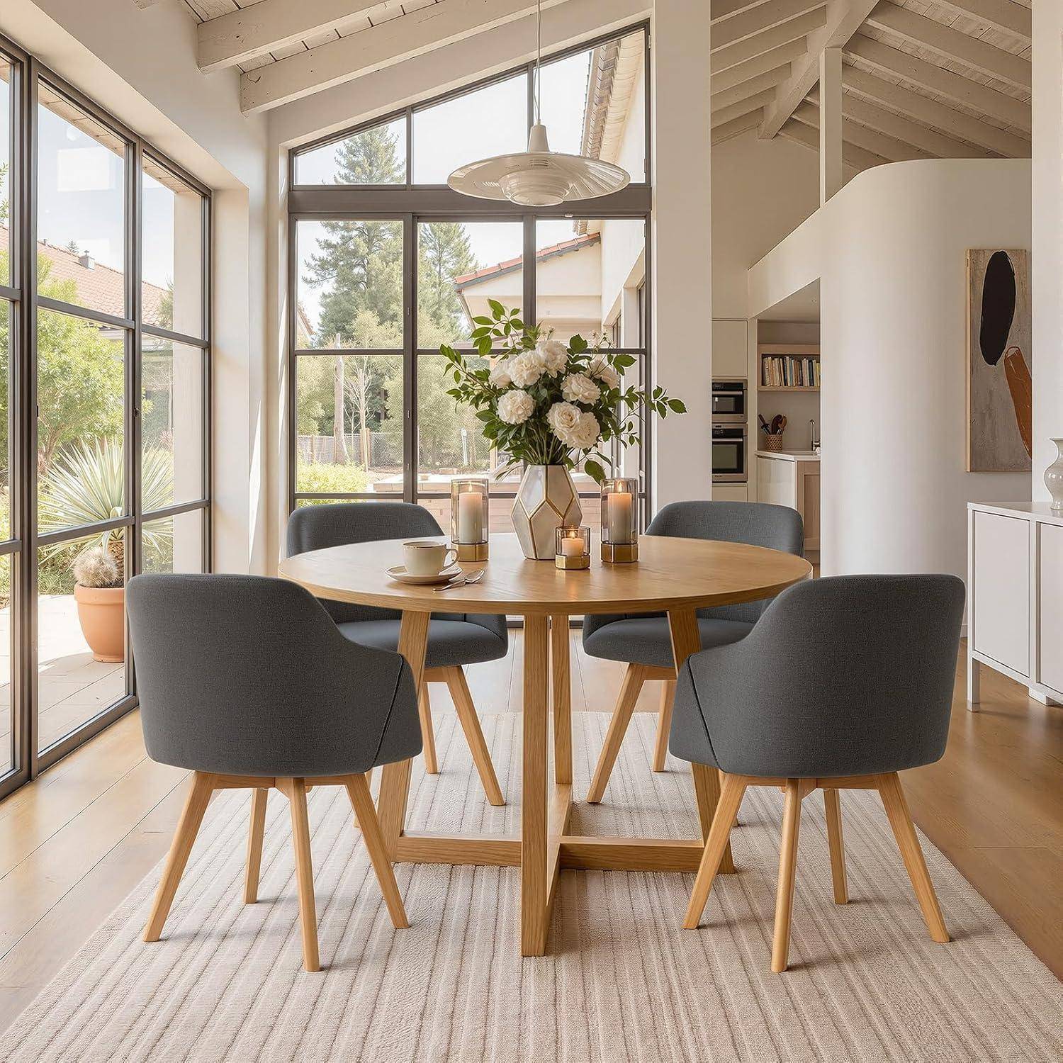 Moderner Essbereich mit einem runden Holztisch, vier grauen Stühlen und einer Vase mit weißen Blumen in einem hellen Raum mit großen Fenstern und einer Treppe.