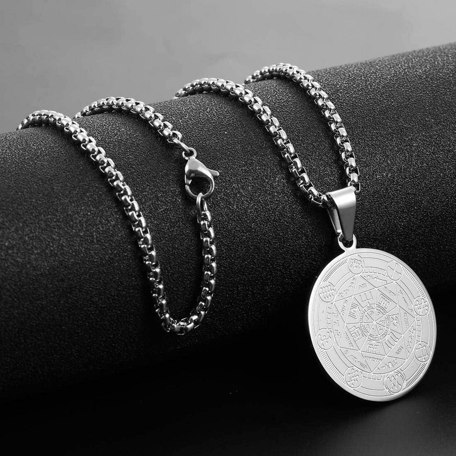 Silberkettenhalsband mit rundem graviertem Anhänger, ausgestellt auf einem schwarzen Ständer.