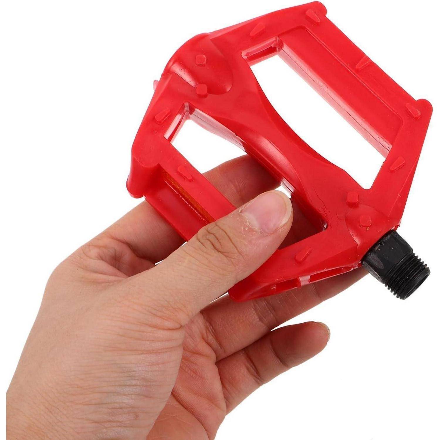 Eine Hand hält ein rotes Kunststoff-Fahrradpedal mit einer schwarzen Gewindeachse vor einem weißen Hintergrund.