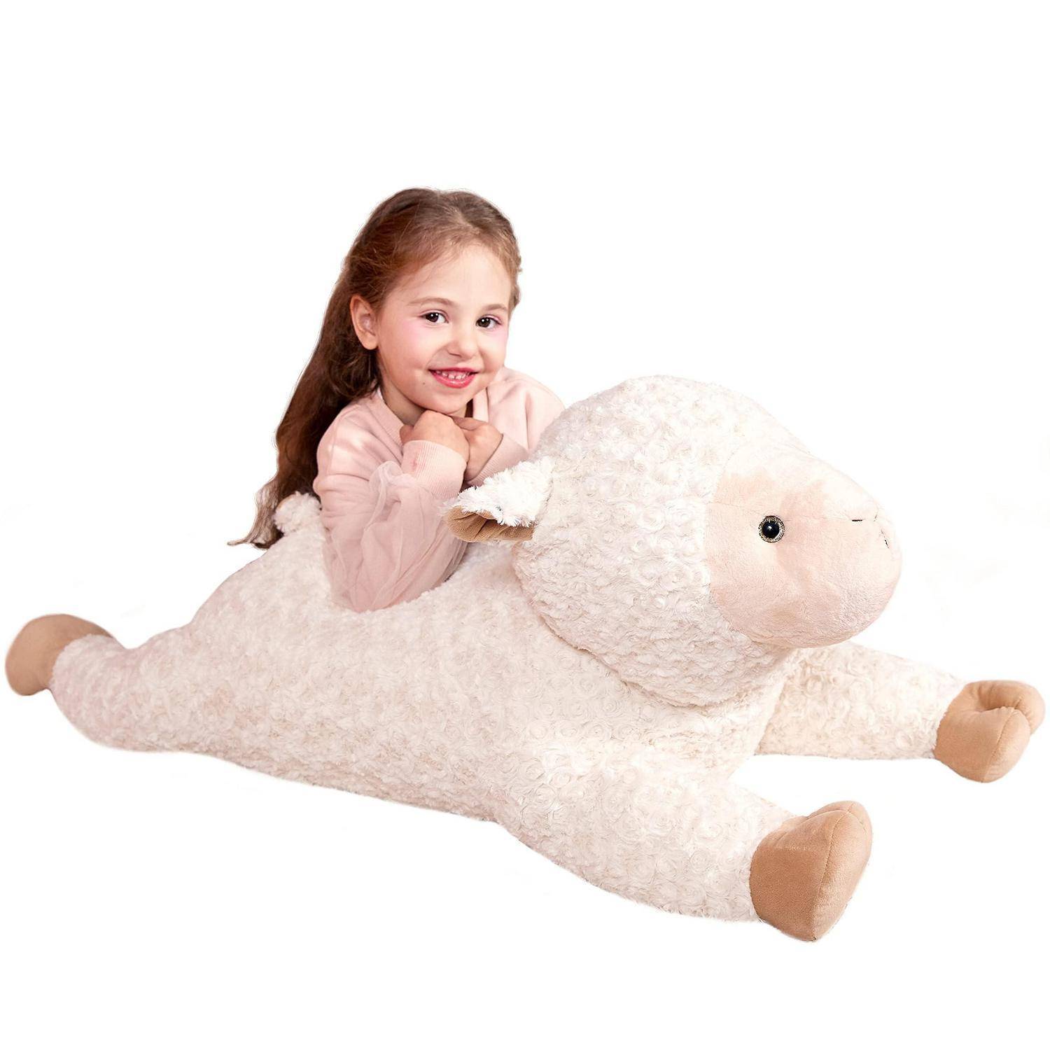 Junges Mädchen lächelnd auf einem großen plüschigen Lamm-Kuscheltier liegend vor weißem Hintergrund.