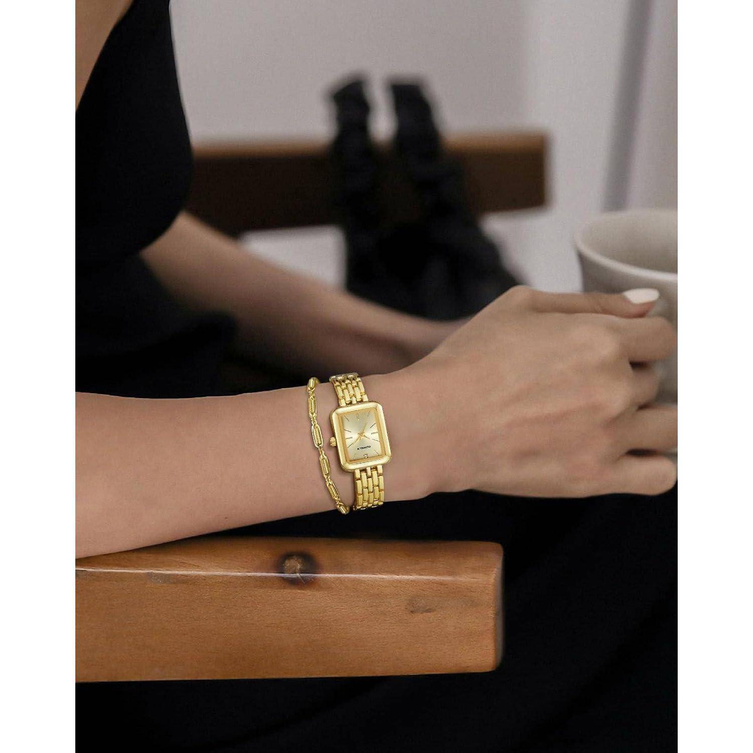 Nahaufnahme des Arms einer Frau mit einer goldenen Armbanduhr und einem Armband, während sie eine Tasse an einem Holztisch hält.