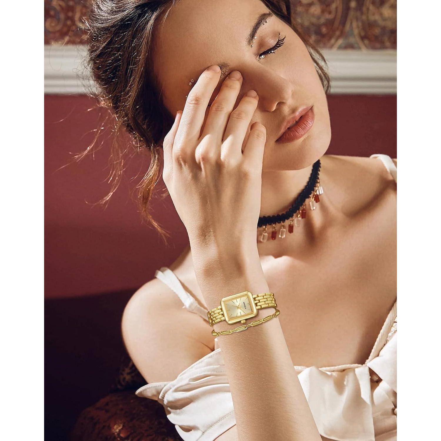 Porträt einer Frau mit geschlossenen Augen, die ihr Gesicht berührt und goldenen Schmuck sowie eine Armbanduhr trägt, posiert vor einem kastanienbraunen Hintergrund.