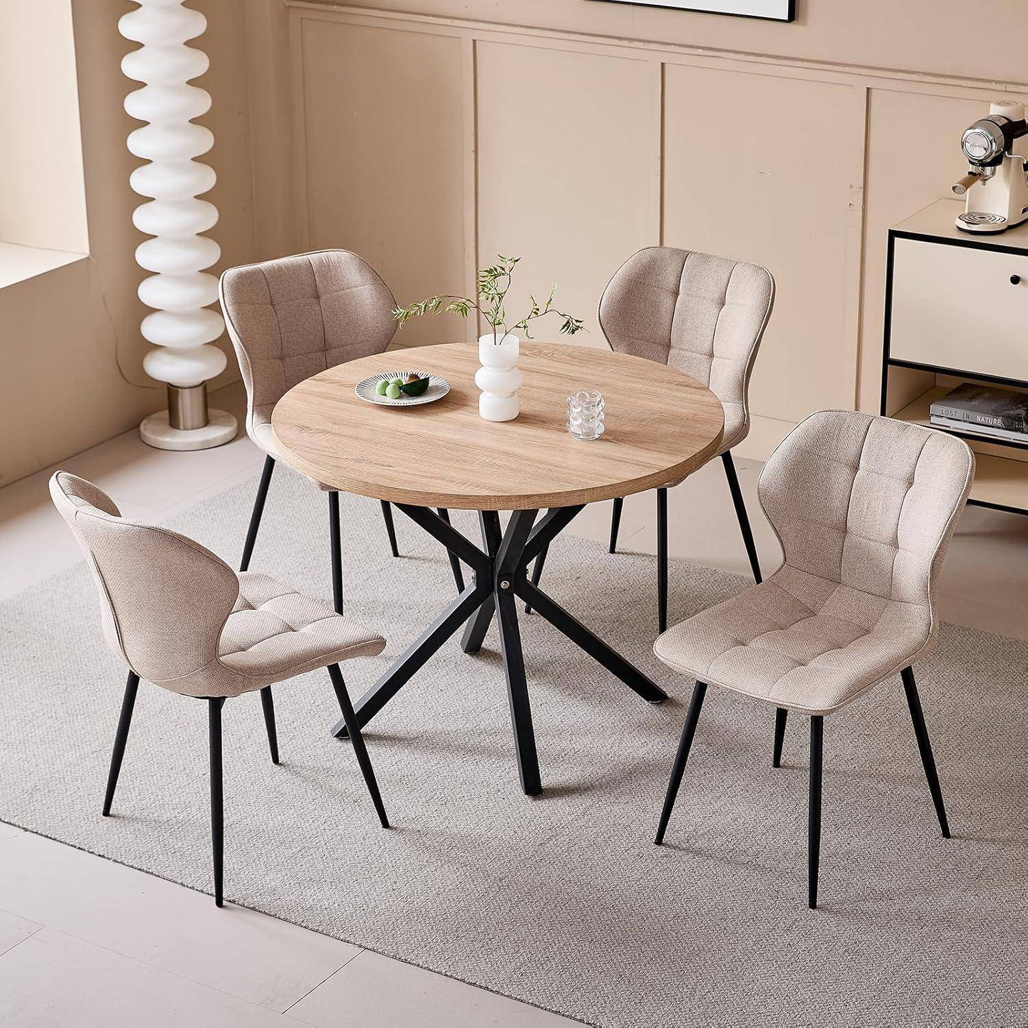 Vier beige gepolsterte Stühle umgeben einen runden Holztisch mit schwarzem Metallgestell auf einem hellen Teppich in einem modernen Esszimmer.