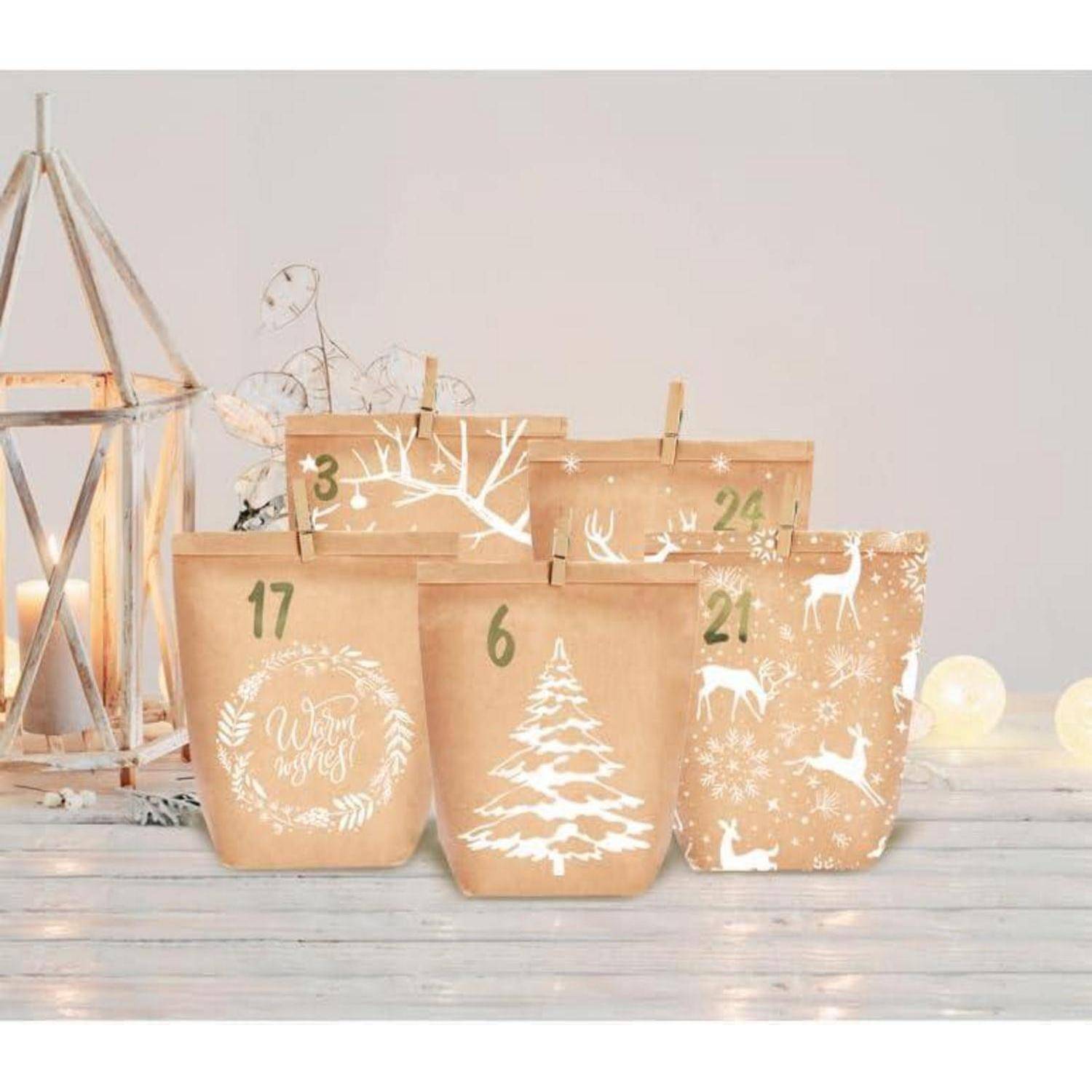 Satz Adventskalender-Geschenktüten aus Kraftpapier mit weißen Winter- und Rentierdesigns, nummeriert für die Tage 3, 6, 17, 21 und 24, auf einer Holzoberfläche.