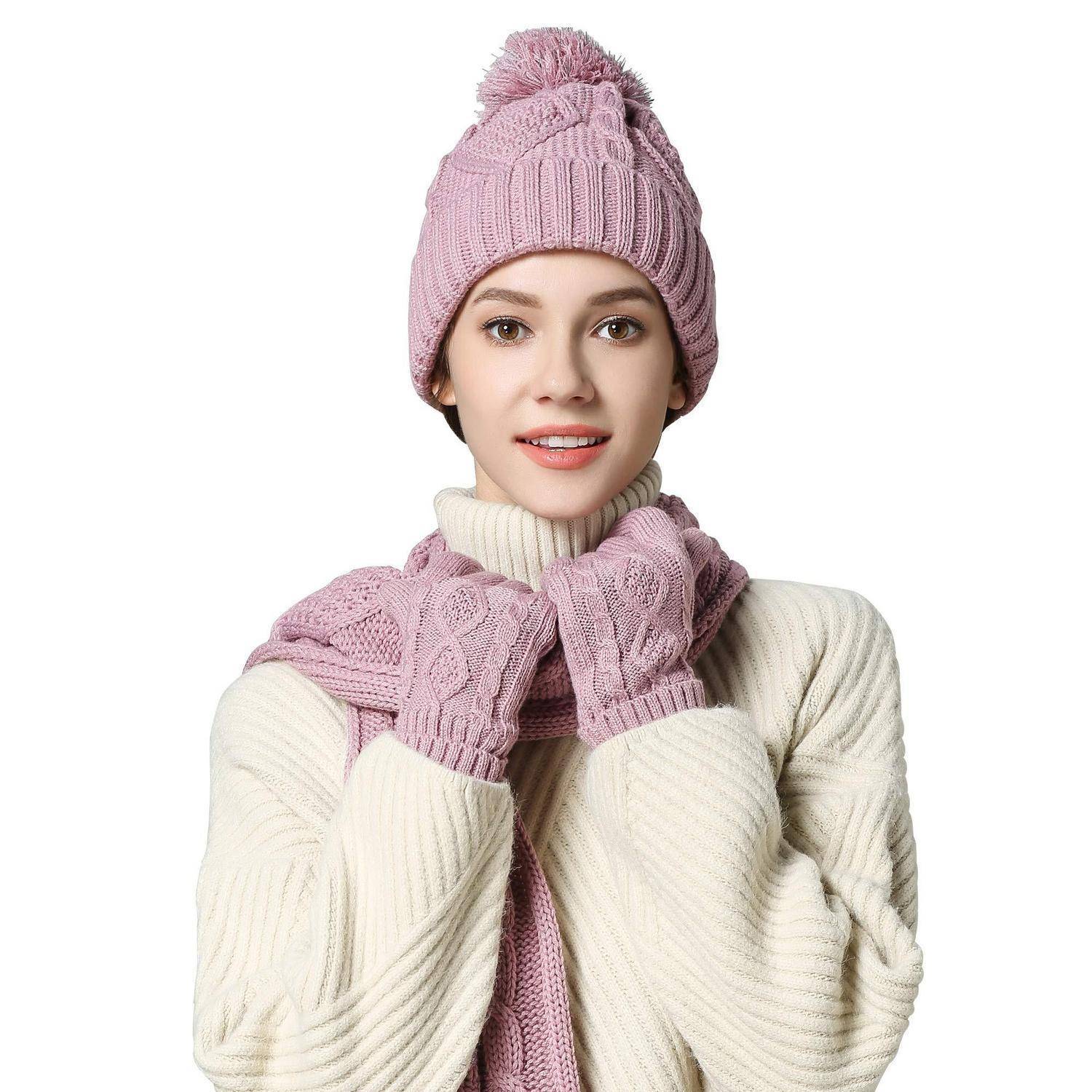 Porträt einer Frau mit einer rosafarbenen Strickmütze, einem Schal und Handschuhen sowie einem cremefarbenen Pullover vor weißem Hintergrund.