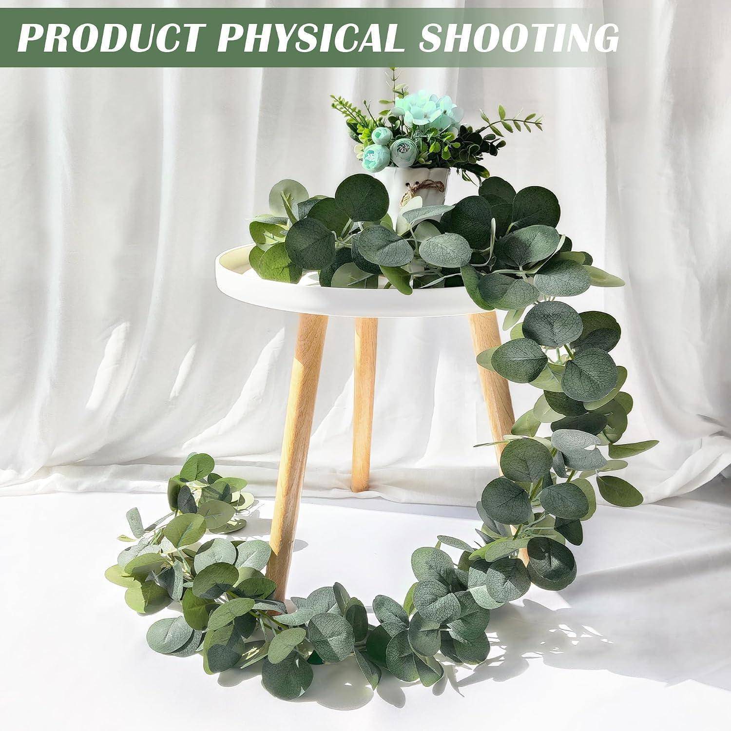 Eukalyptusgirlande, die um einen kleinen weißen Tisch drapiert ist, mit einer Blumengestaltung oben darauf, als Produktfoto vor weißem Hintergrund dargestellt.