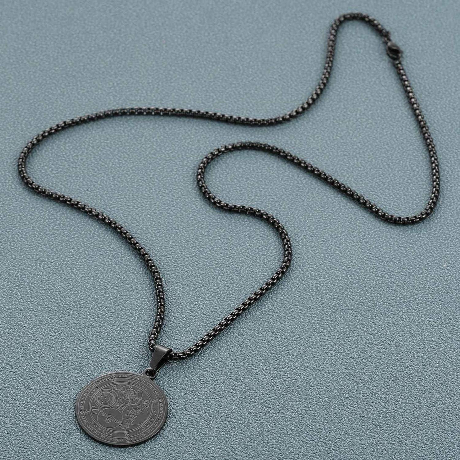 Schwarze Kettenkette mit rundem graviertem Anhänger auf grauem Hintergrund.