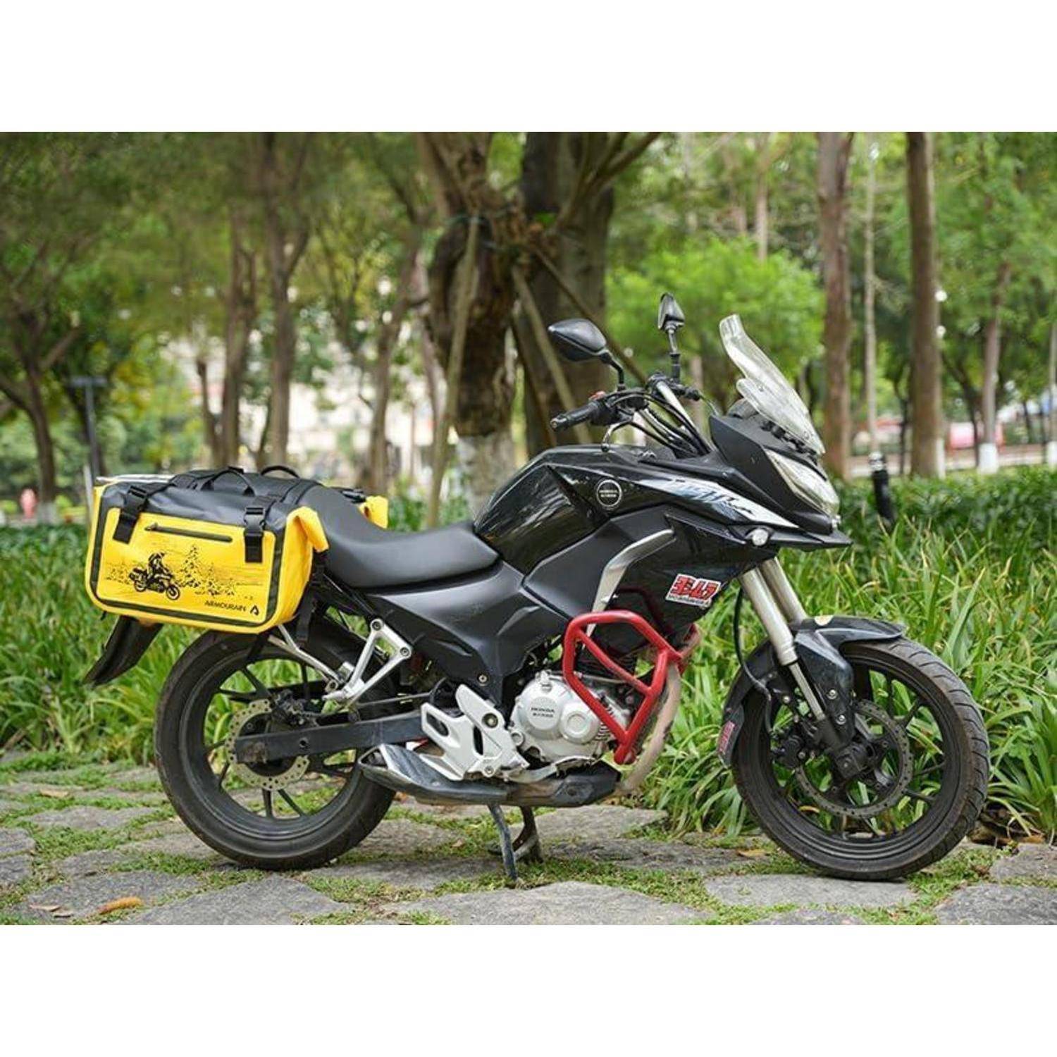 Schwarzes Adventure-Motorrad auf einem Steinweg in einem Park geparkt, mit einer gelben Seitentasche an der Hinterseite angebracht.