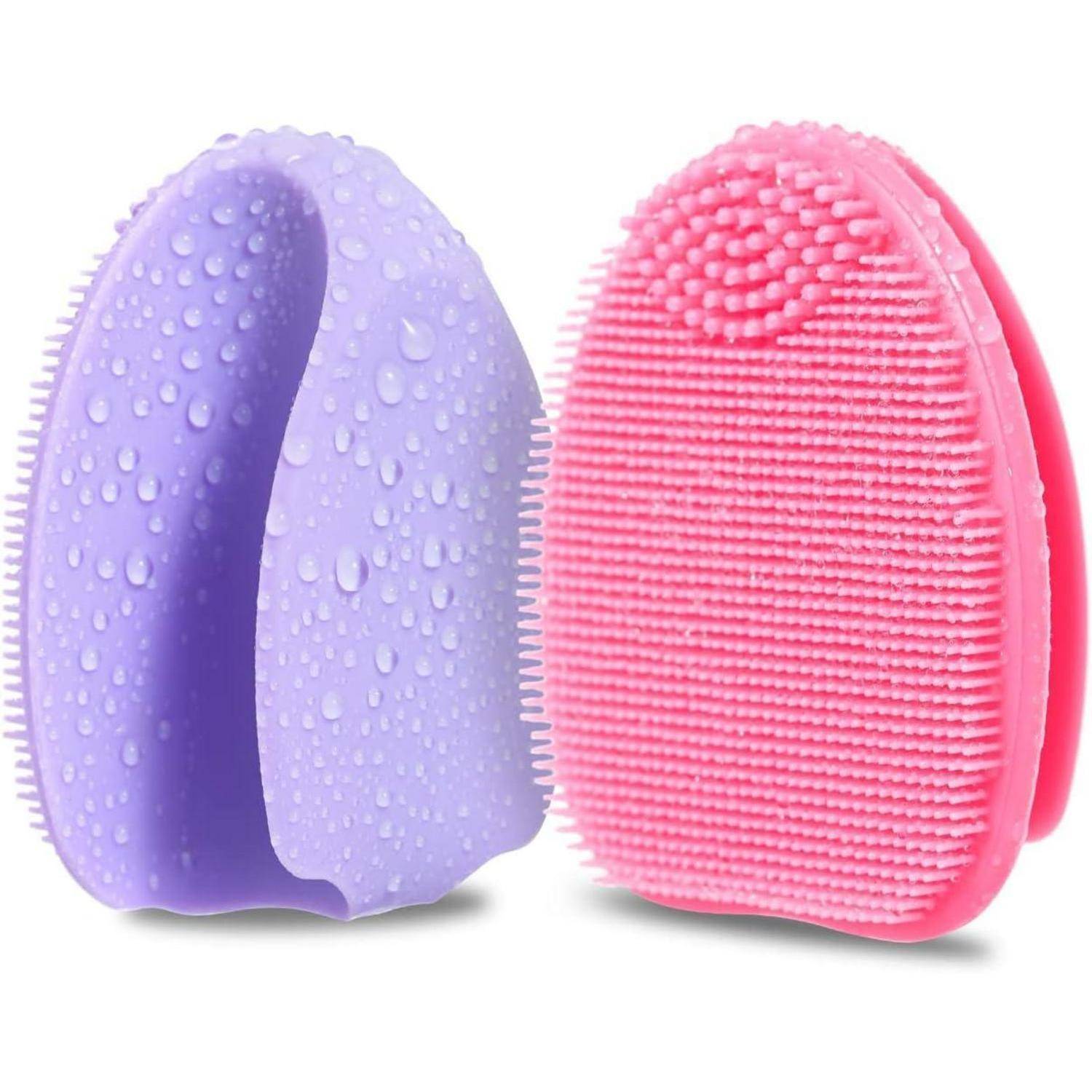 Zwei Gesichtsreinigungsbürsten aus Silikon, eine violett und eine rosa, mit strukturierten Borsten und Wassertropfen auf weißem Hintergrund.