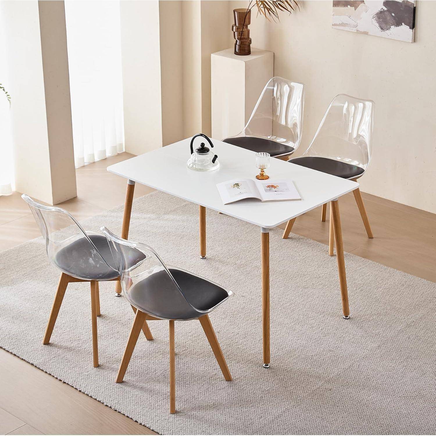 Modernes Esszimmerset mit einem weißen rechteckigen Tisch, vier transparenten Stühlen und einem hellen Teppich in einem hellen minimalisti­schen Raum.